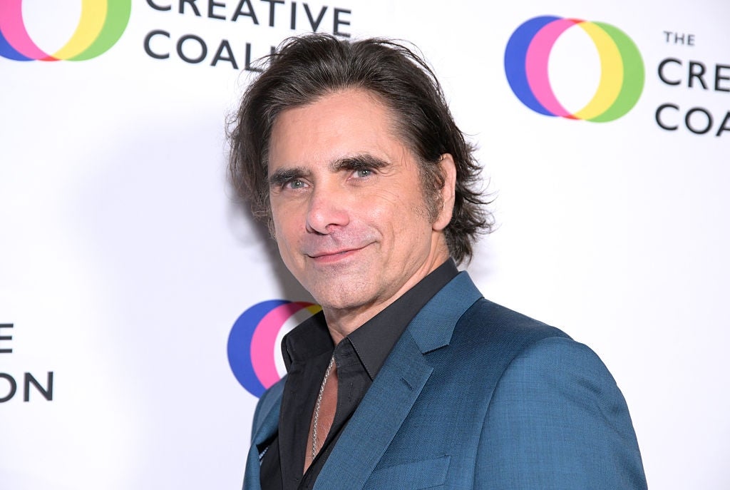 Celebrity in a tailored suit with a confident smile at a media event backdrop