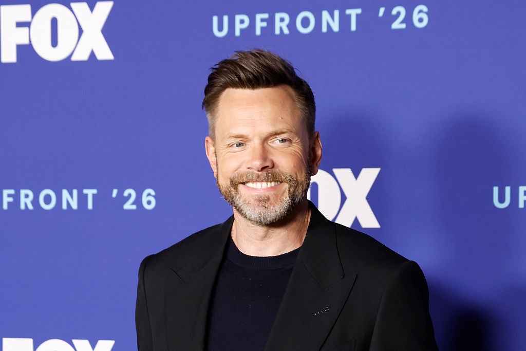 Man on a red carpet wearing a dark blazer over a black shirt, smiling in front of a media backdrop with "Upfront '26" and "Fox" logos