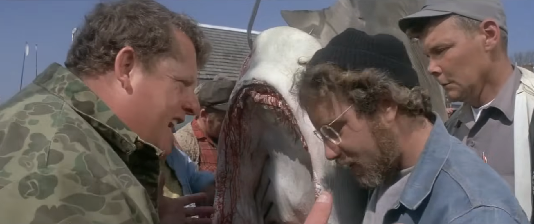 People discuss around a captured shark in a scene from a movie, showcasing tense expressions and focused attention