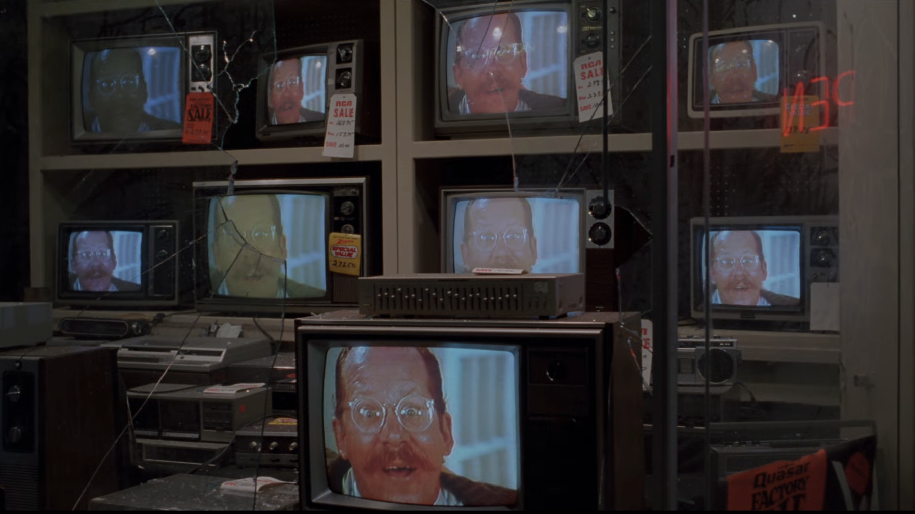 Multiple vintage TVs display the same mustachioed man's face in an electronics store
