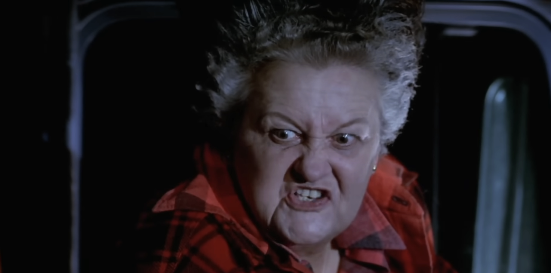 A person with a fierce expression wearing a plaid shirt is seen in a close-up, possibly from a movie or TV scene