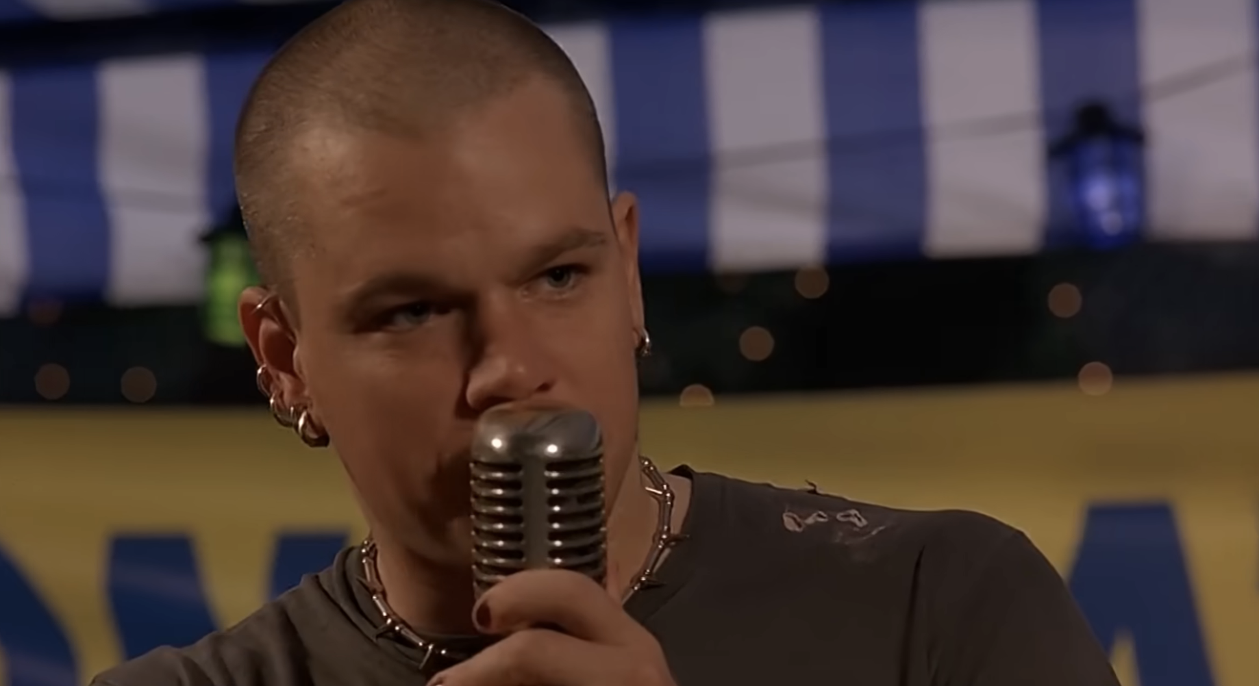 Person holding a vintage microphone, performing in a scene; wearing a casual, edgy outfit with accessories