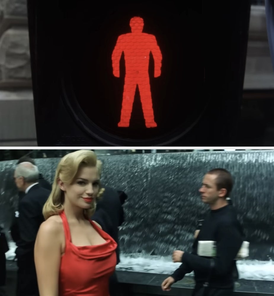 A red pedestrian crossing signal above; a person in a vintage-style elegant outfit poses near a fountain with passing bystanders