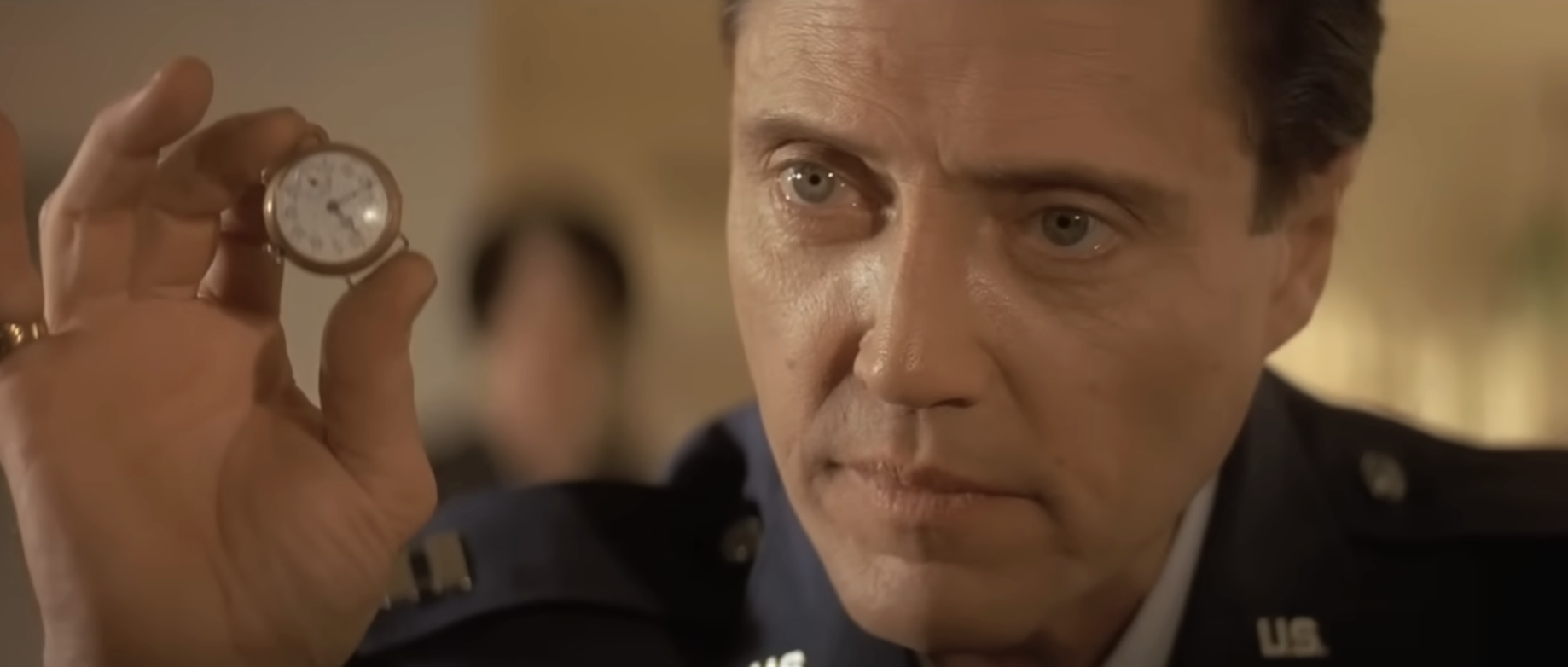 Person in military uniform holds a small, round object, staring intently, suggesting a dramatic scene