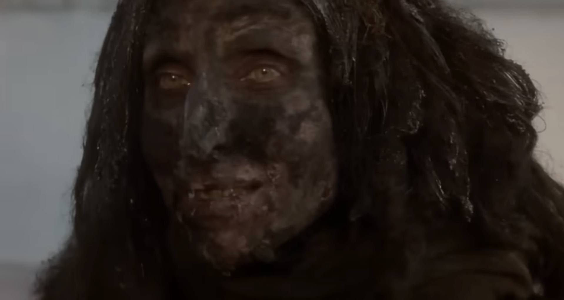 Character from a movie with dark, weathered skin and long hair, conveying a rugged, intense appearance