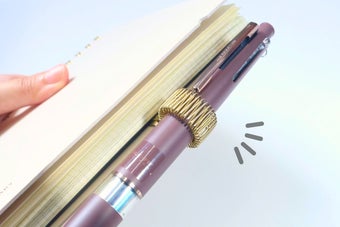 ノートページを挟んだペン。ペンには金色のスプリングが巻かれている。