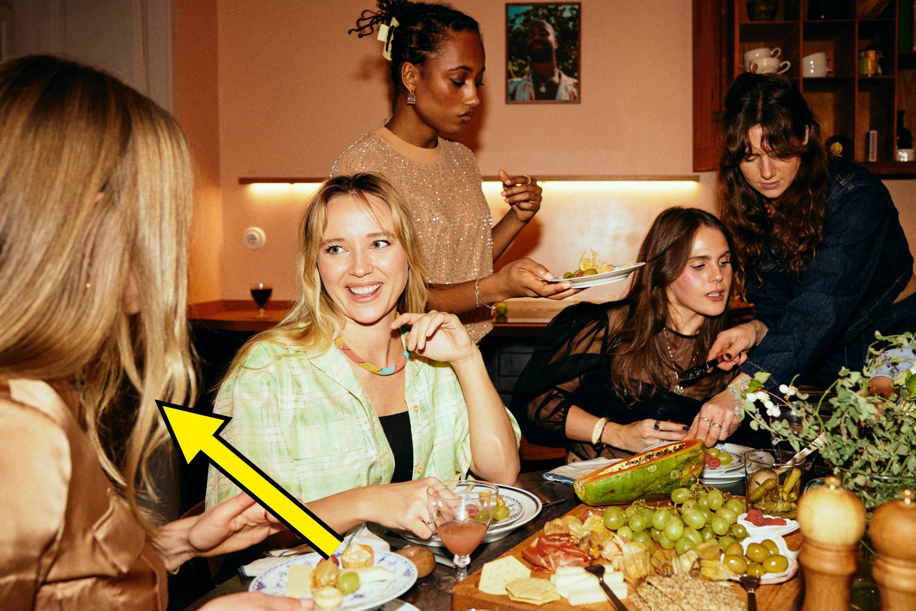 A group of women gathers at a dinner party and enjoys a spread of charcuterie. Text: "If you're really a girls' girl, you don't have to convince everyone you are one."