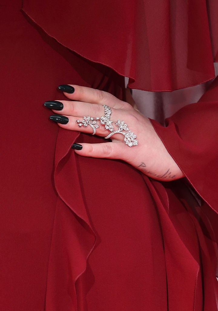 Close-up of a celebrity's hand on a red carpet, featuring black nails and a statement ring with an intricate floral design