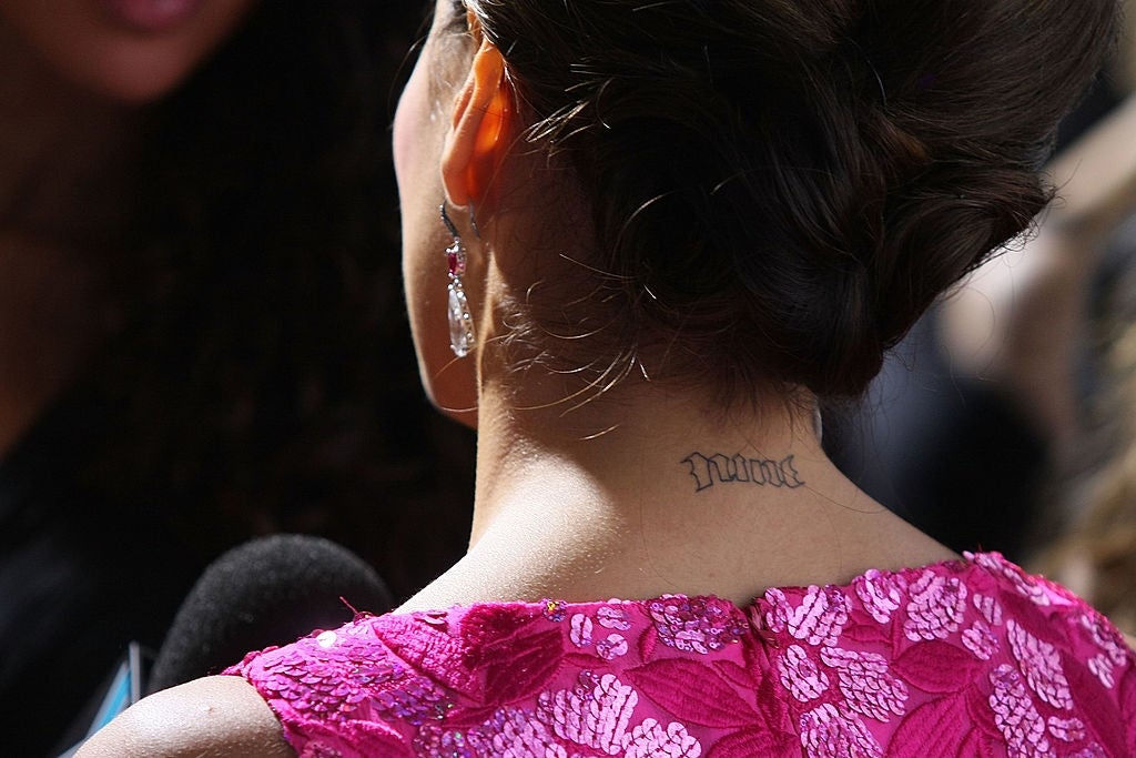 Celebrity on red carpet with an elegant updo and an intricate pink lace dress, showing a neck tattoo during an interview