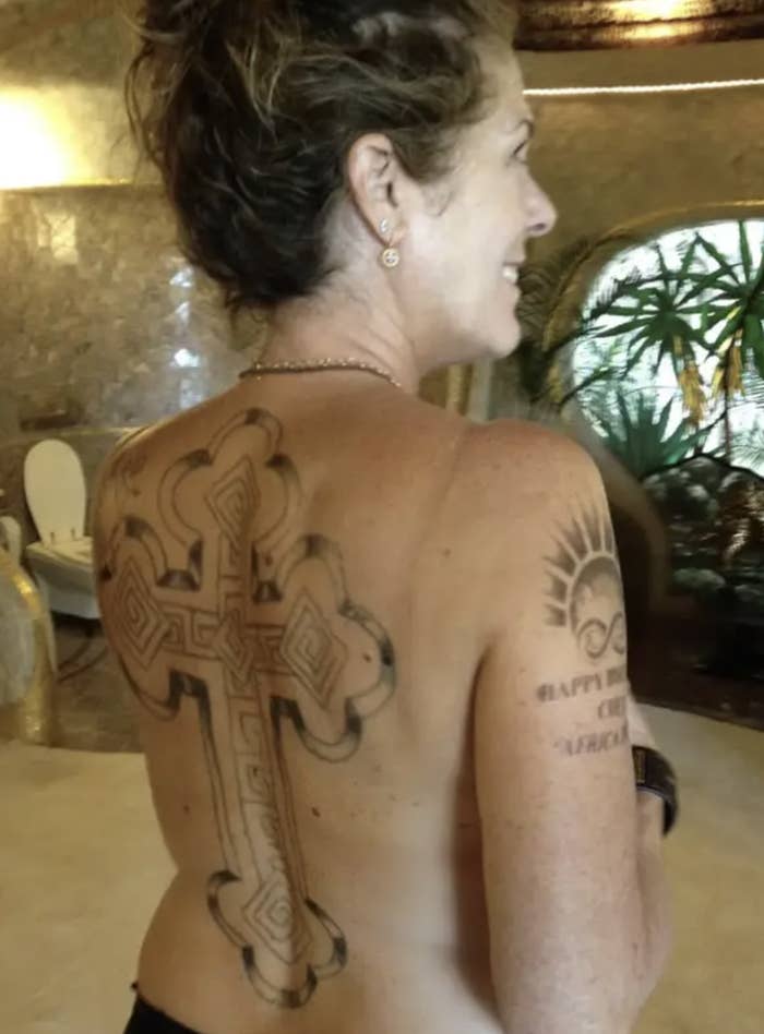 Person showing detailed cross tattoo on back, smiling, with another tattoo on arm reading "Happy New Year March 2016."