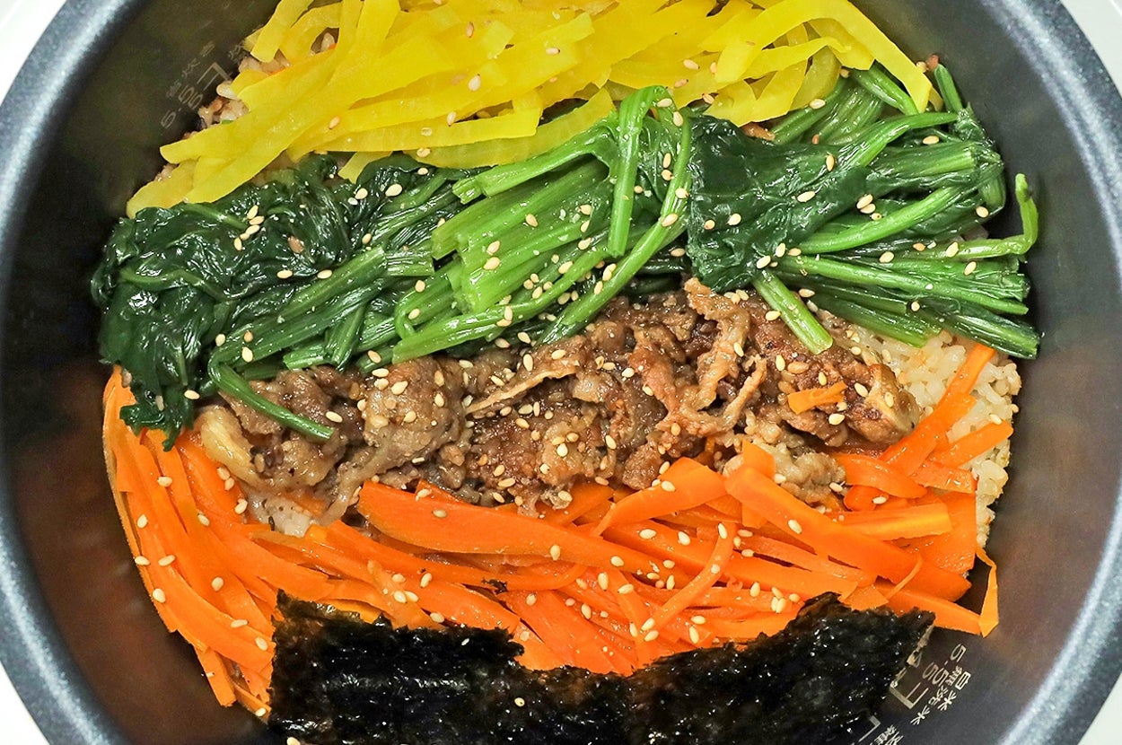 ビビンバが炊飯器の中に盛り付けられている。野菜と肉がご飯の上に並び、ゴマが振りかけられている。