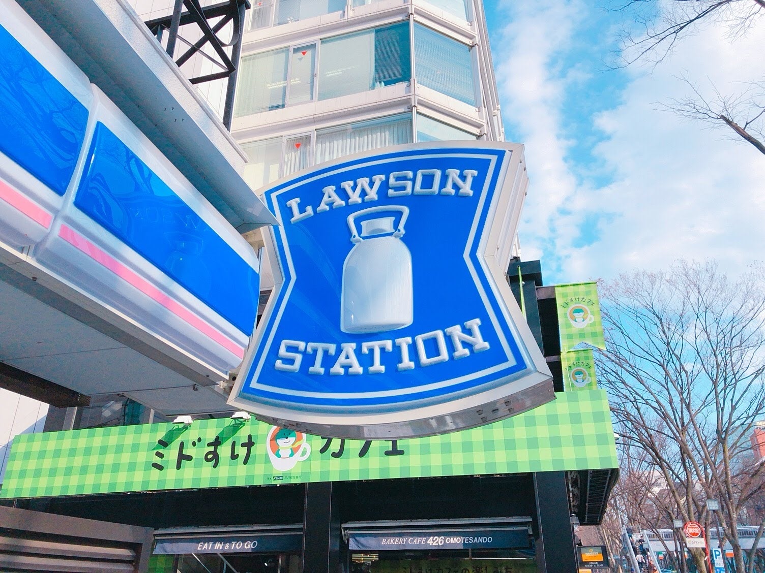 ローソンの店舗サインが建物の前に掲示されています。背景にはビルと木が見えます。