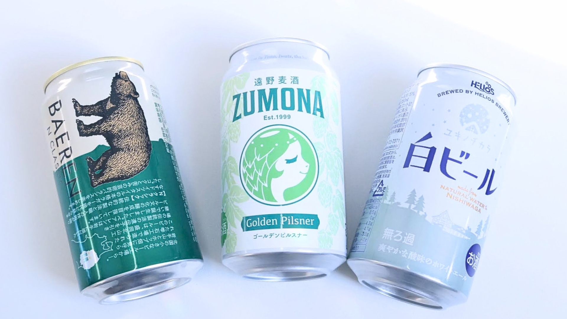 3種類のクラフトビール缶が並んでいる。左から熊のイラスト、緑のラベル、風景のデザイン。