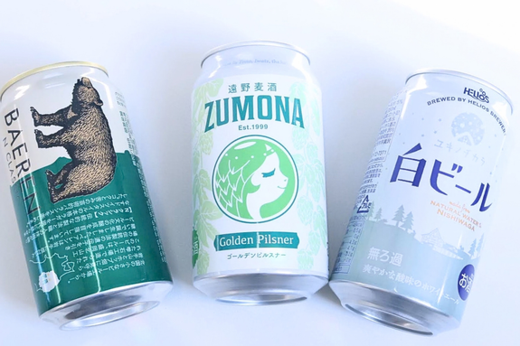 3種類のクラフトビール缶が並んでいる。左から熊のイラスト、緑のラベル、風景のデザイン。