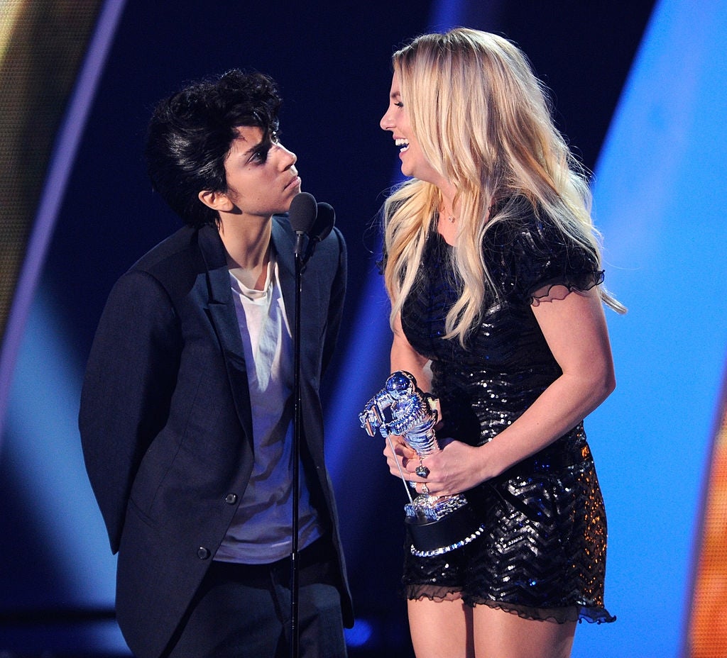 Two people on stage, one in a suit and the other in a sequin dress, sharing a playful moment