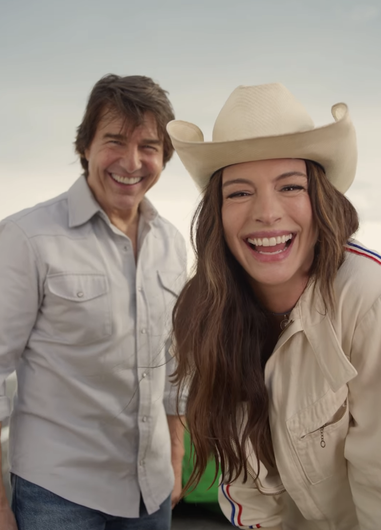Two people smiling outdoors, one wearing a cowboy hat and casual jacket, the other in a casual button-up shirt