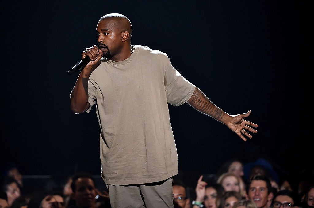 A man on stage holding a microphone, wearing a loose-fitting shirt and pants, speaking to an audience