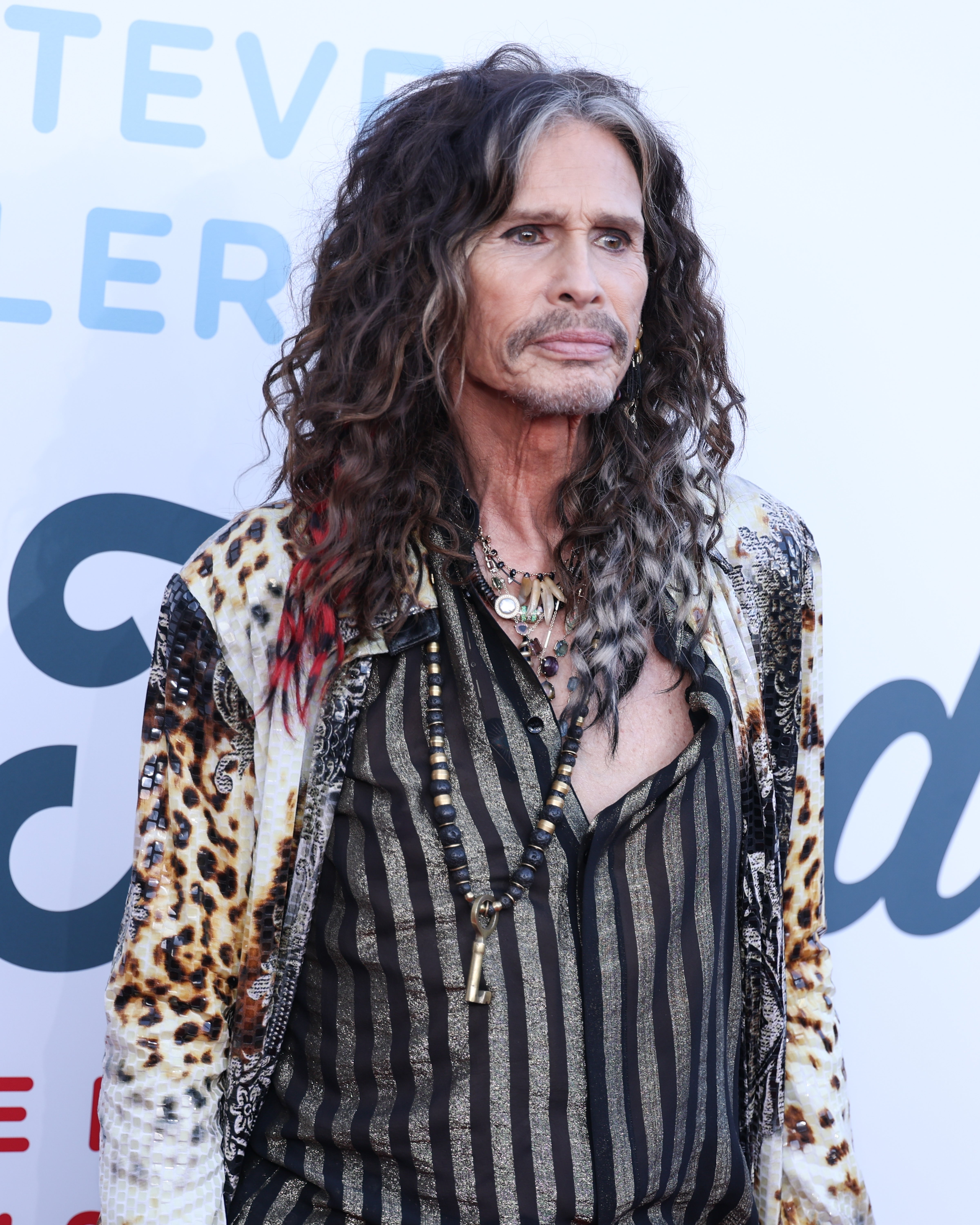 Person with long hair wearing a patterned jacket and striped shirt at a red carpet event