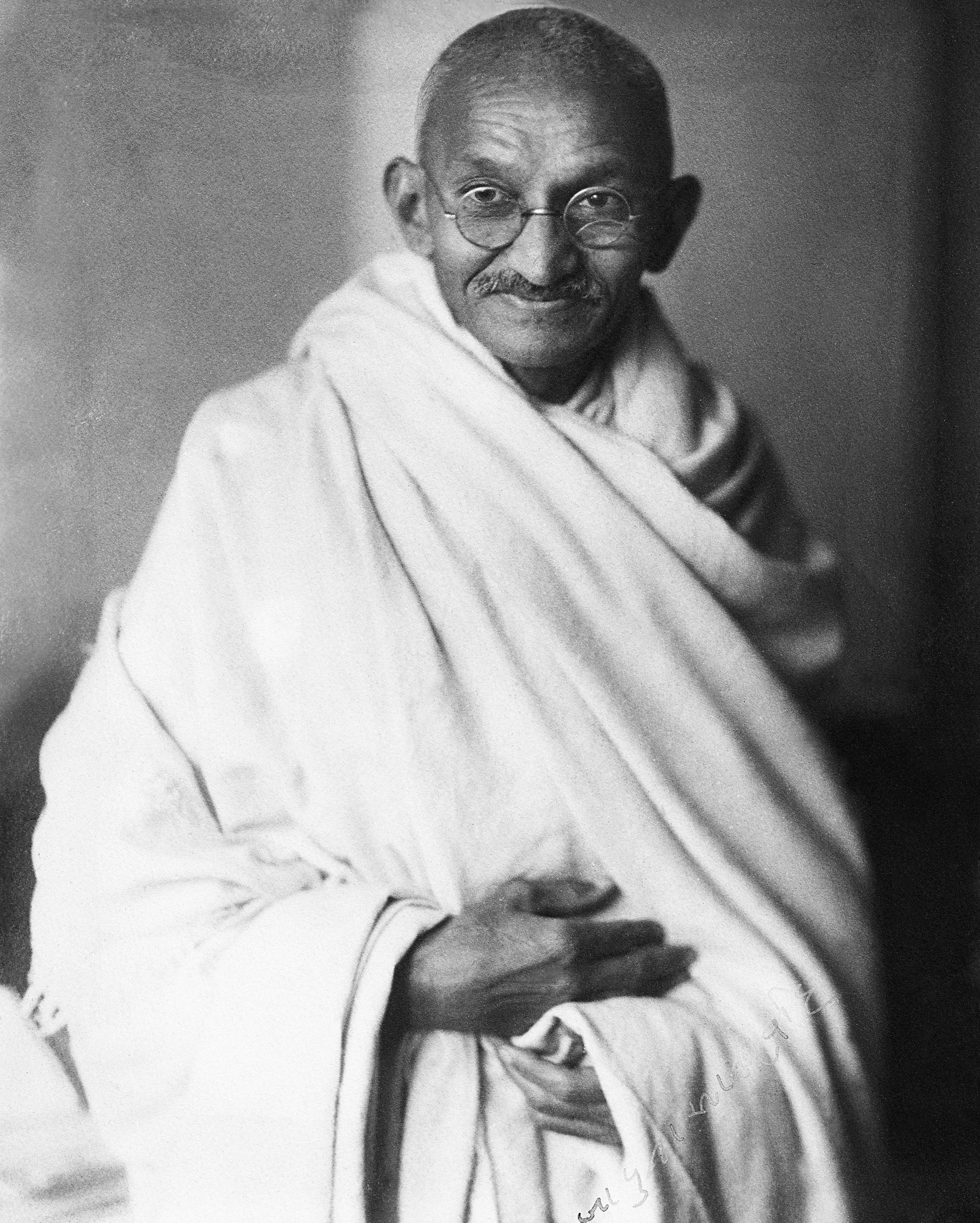 An individual wearing a traditional draped robe and round glasses, with a gentle expression