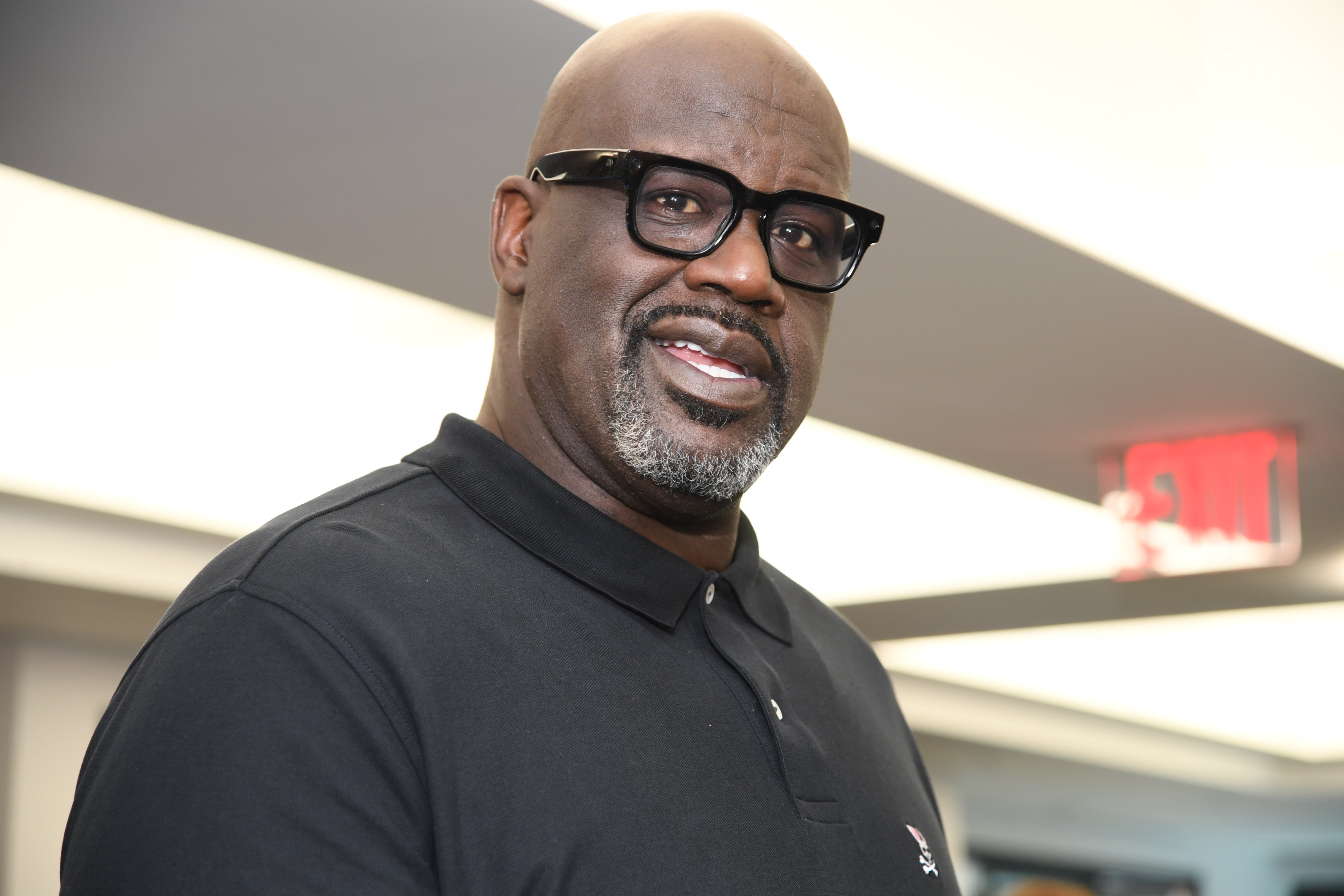 Person in a black polo shirt and glasses smiles at the camera indoors