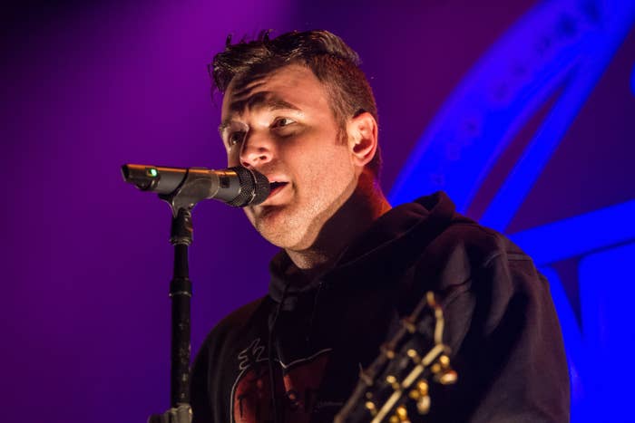 A musician singing passionately into a microphone while playing guitar on stage