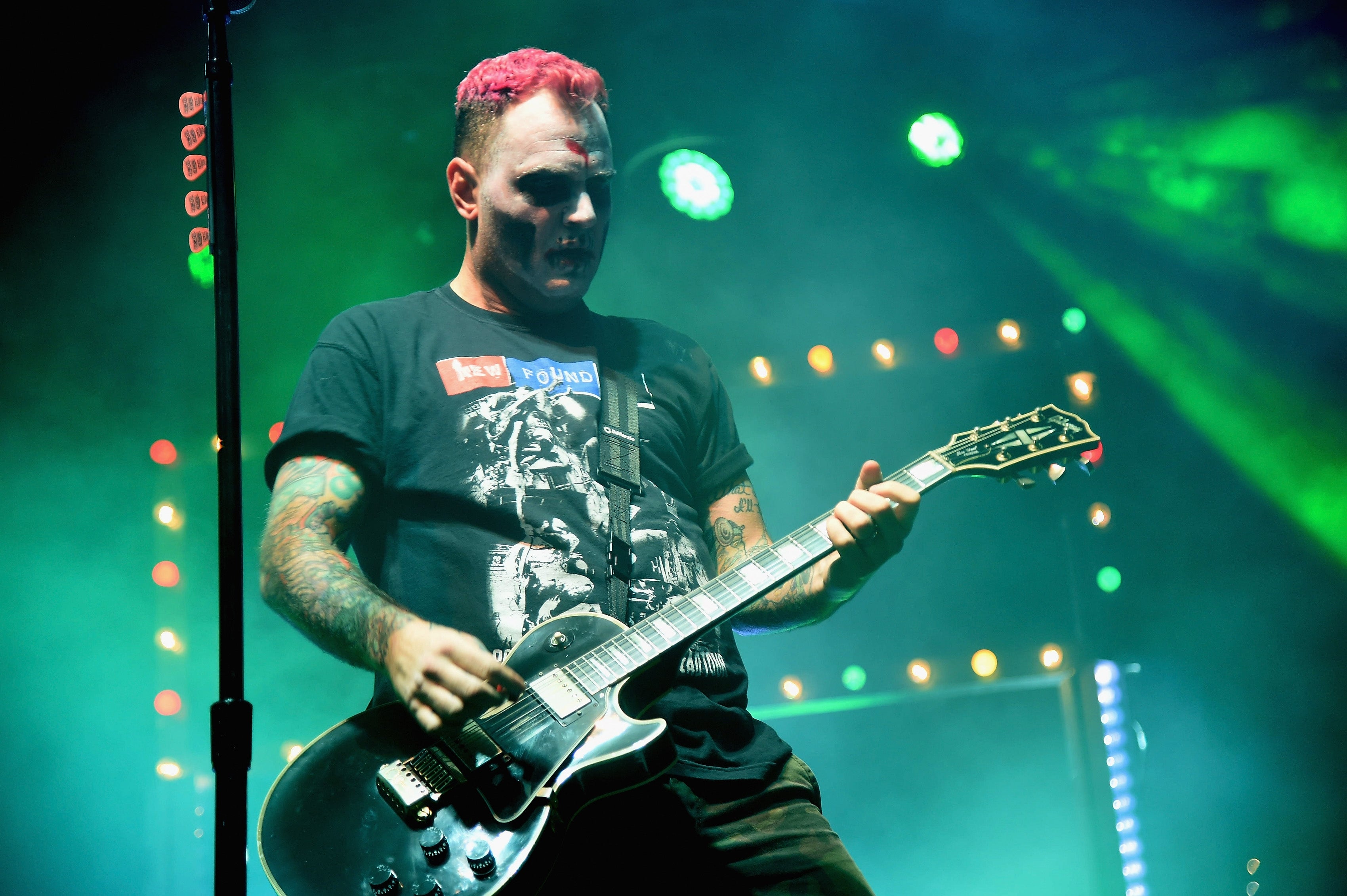Musician playing electric guitar on stage, wearing a graphic t-shirt, with bright lights in the background