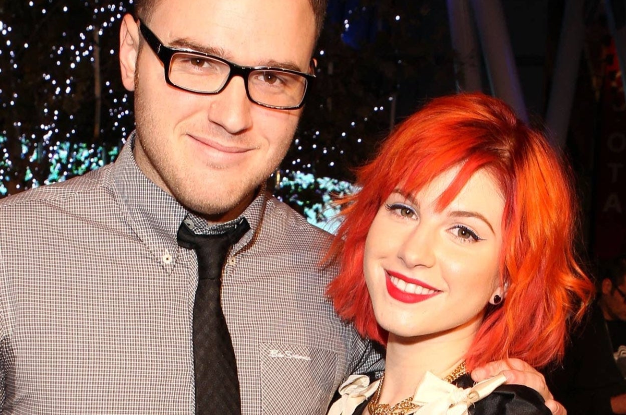 Two people smiling, one with glasses and a tie, the other with bright hair and bold makeup, posing together at an event