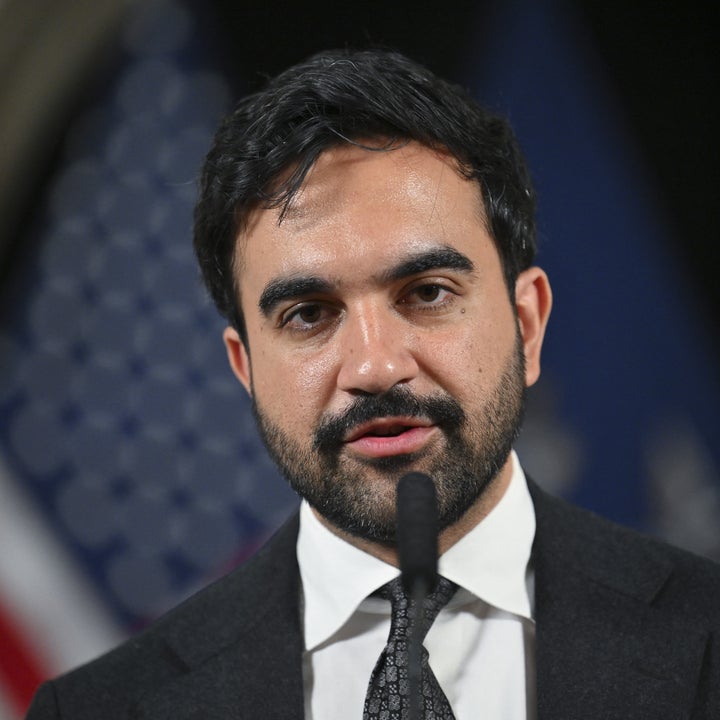 A man in a suit and tie speaks at a podium with a U.S. flag in the background