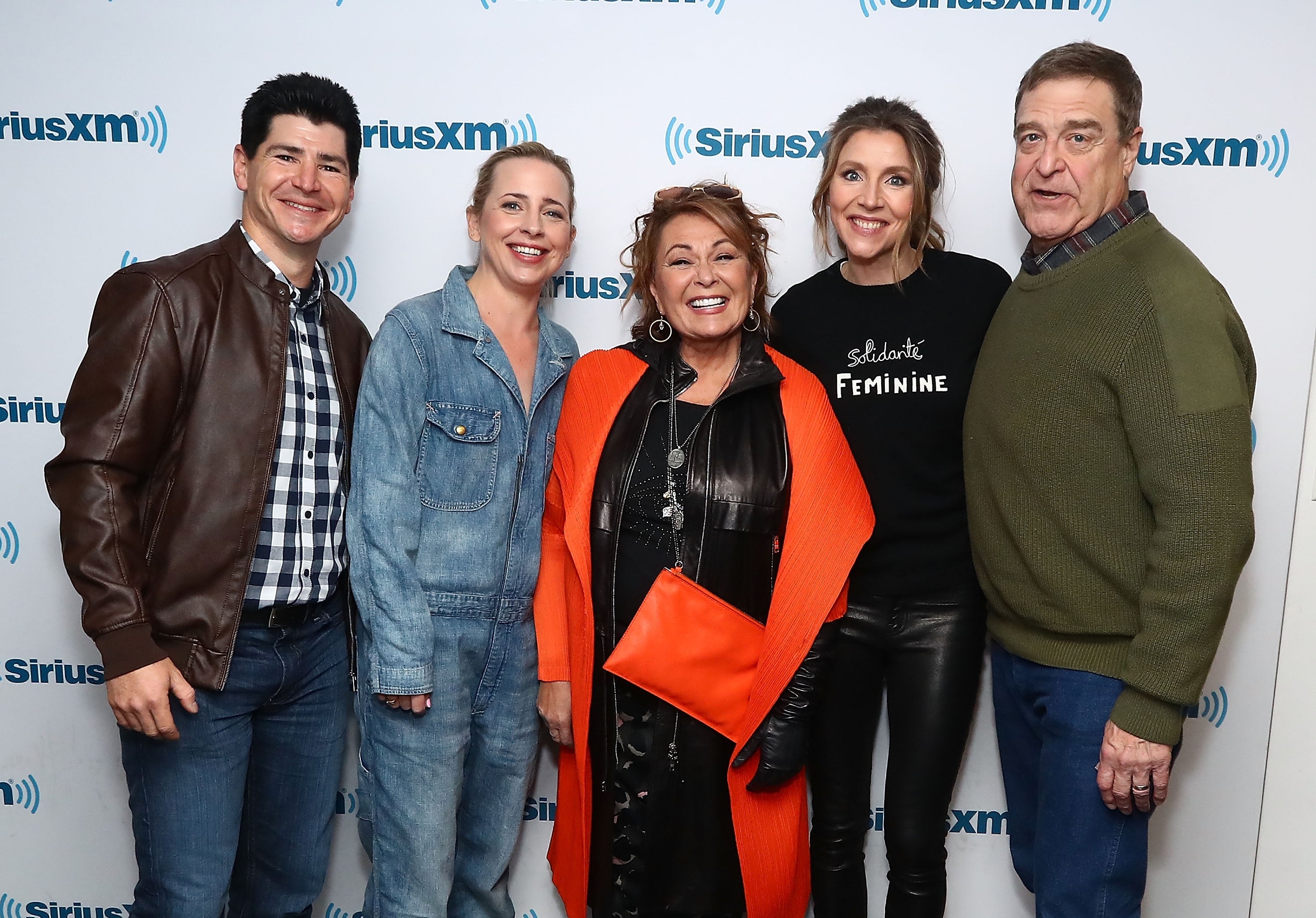 Group photo of five people at a SiriusXM event, casual attire. One wears an orange coat with a bright purse, another a leather jacket