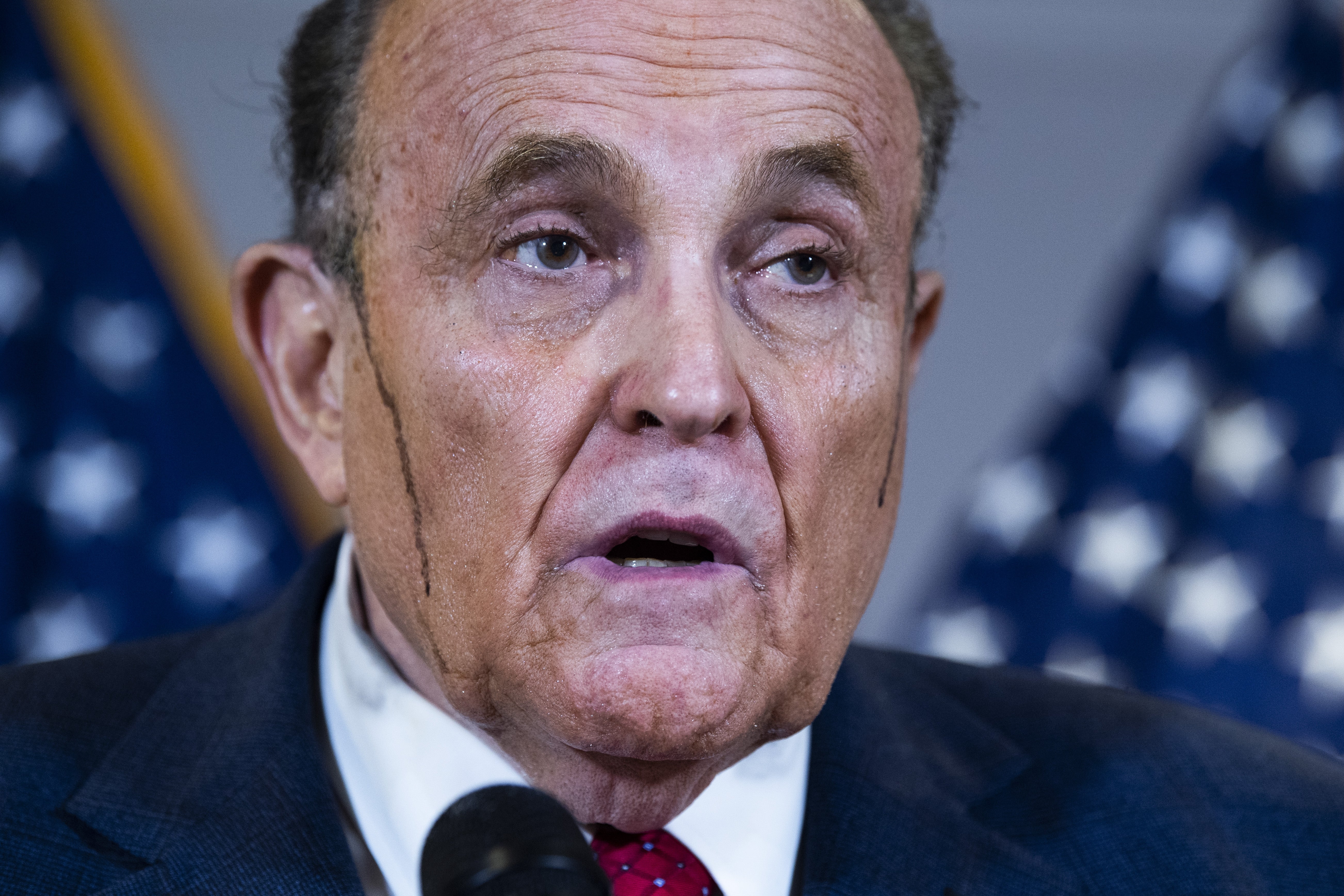 Rudy Giuliani i dress taler ved et podium med amerikanske flagg i bakgrunnen