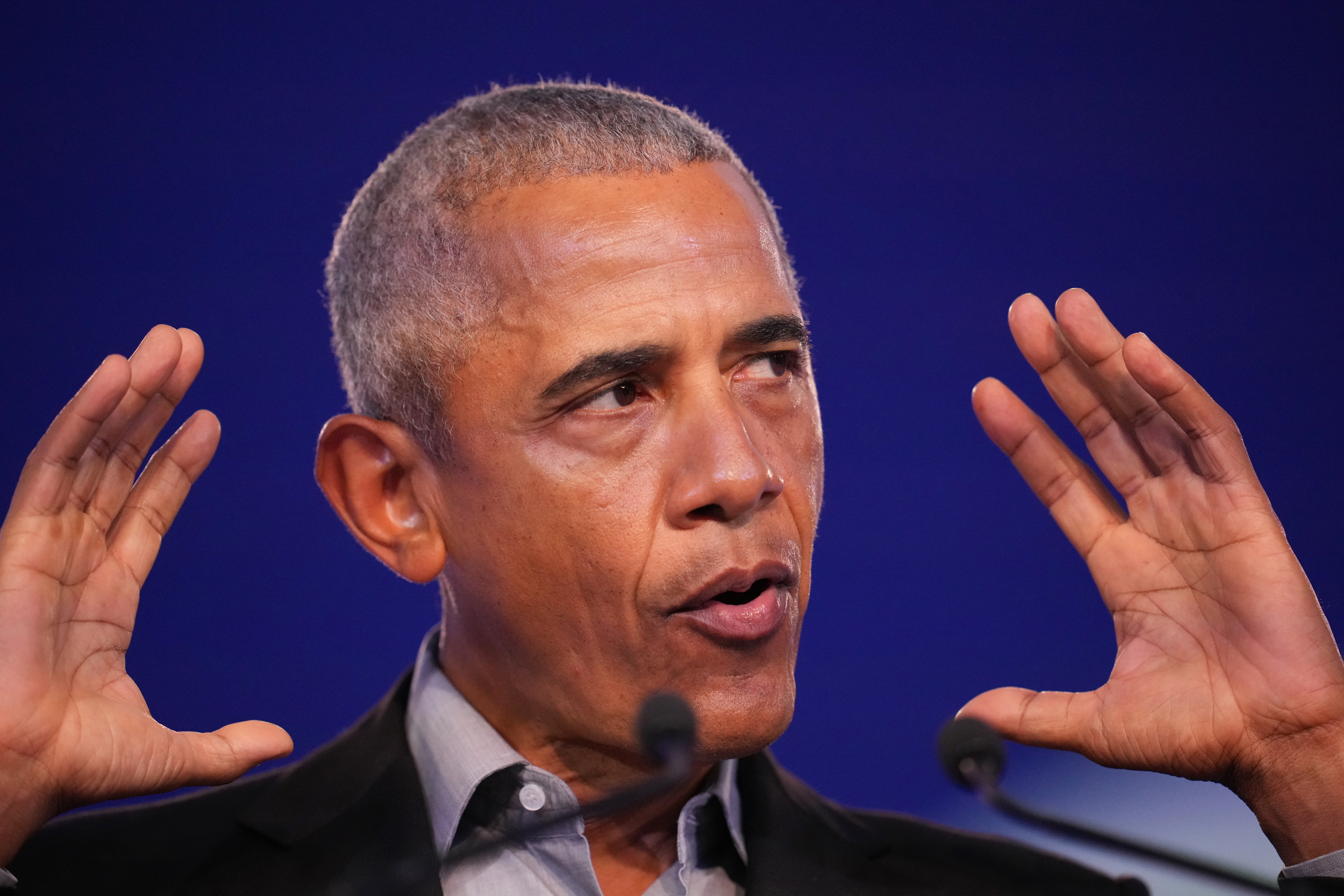 Obama snakker med uttrykksfulle hender hevet nær ansiktet, iført skjorte med krage og blazer