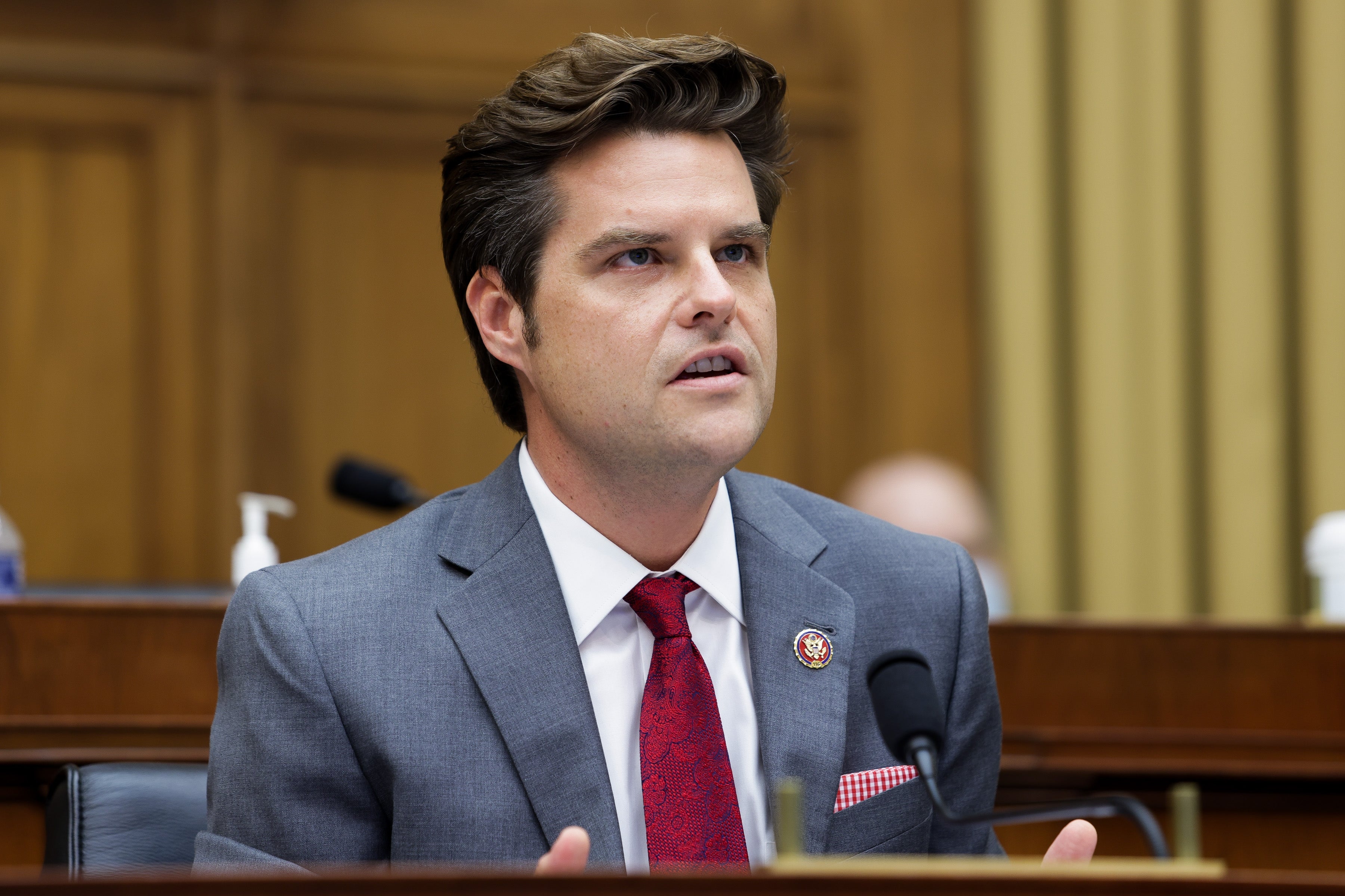 Matt Gaetz i dress snakker lidenskapelig på en formell begivenhet, sittende bak en mikrofon