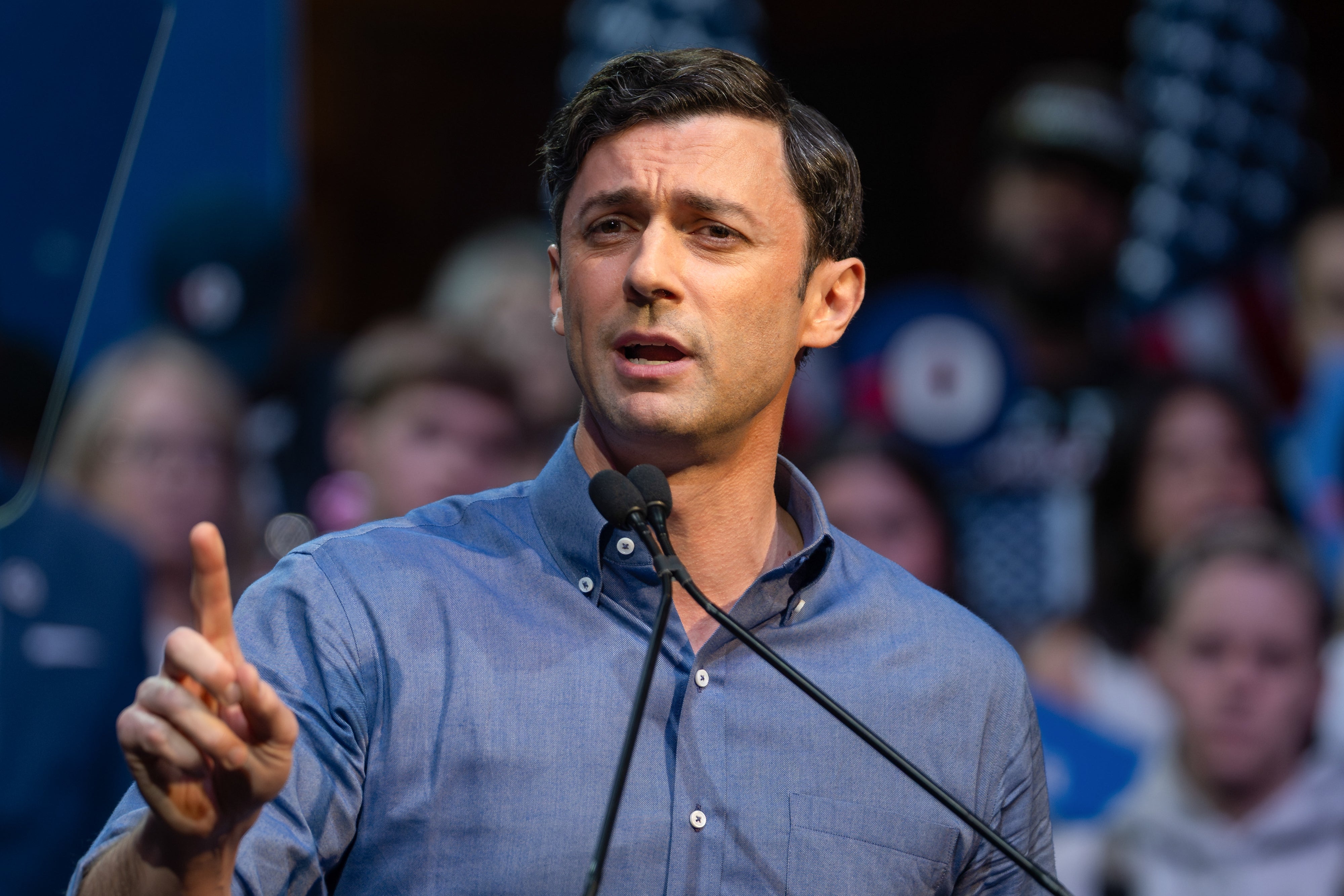Jon Ossoff i blå skjorte snakker lidenskapelig ved et podium og gestikulerer med hånden. Et publikum er synlig i bakgrunnen