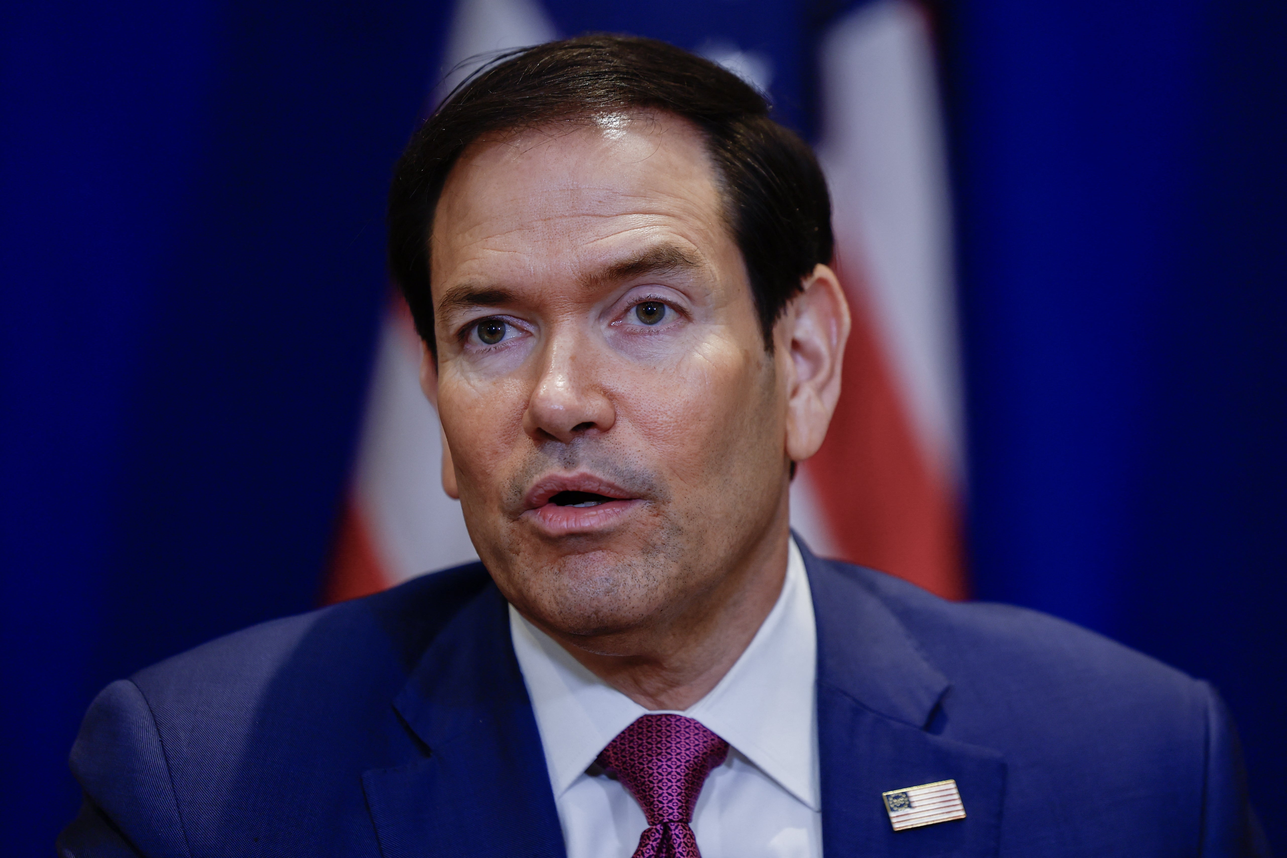 Marco Rubio i dress snakker på et arrangement med flagg i bakgrunnen