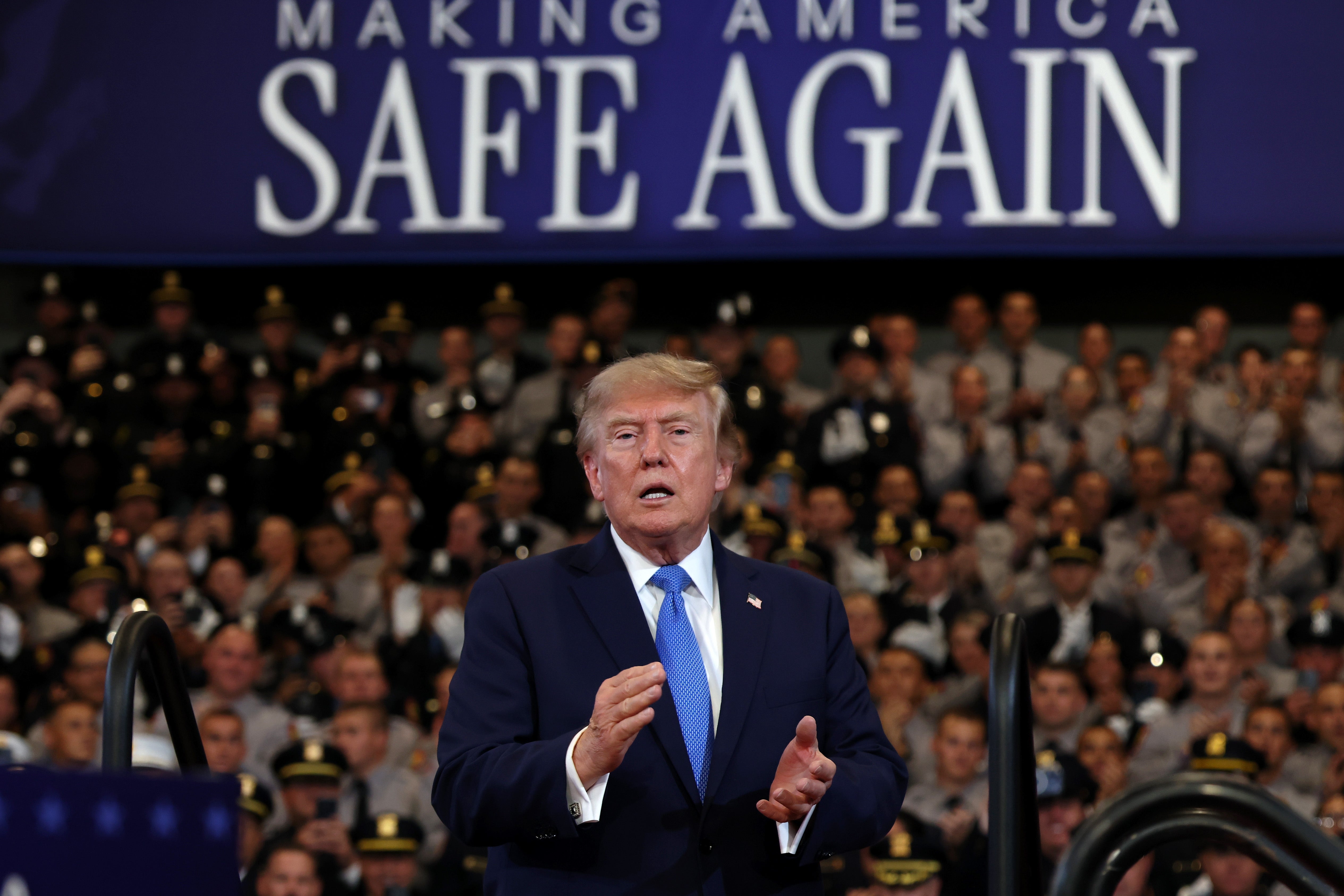 Donald Trump taler på scenen foran et publikum av uniformerte offiserer, med et banner med teksten «Making America Safe Again»; over