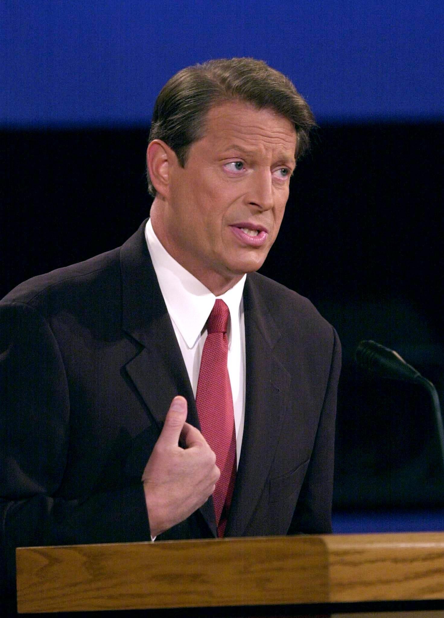 Al Gore-person i dress snakker ved et podium og gestikulerer med hånden