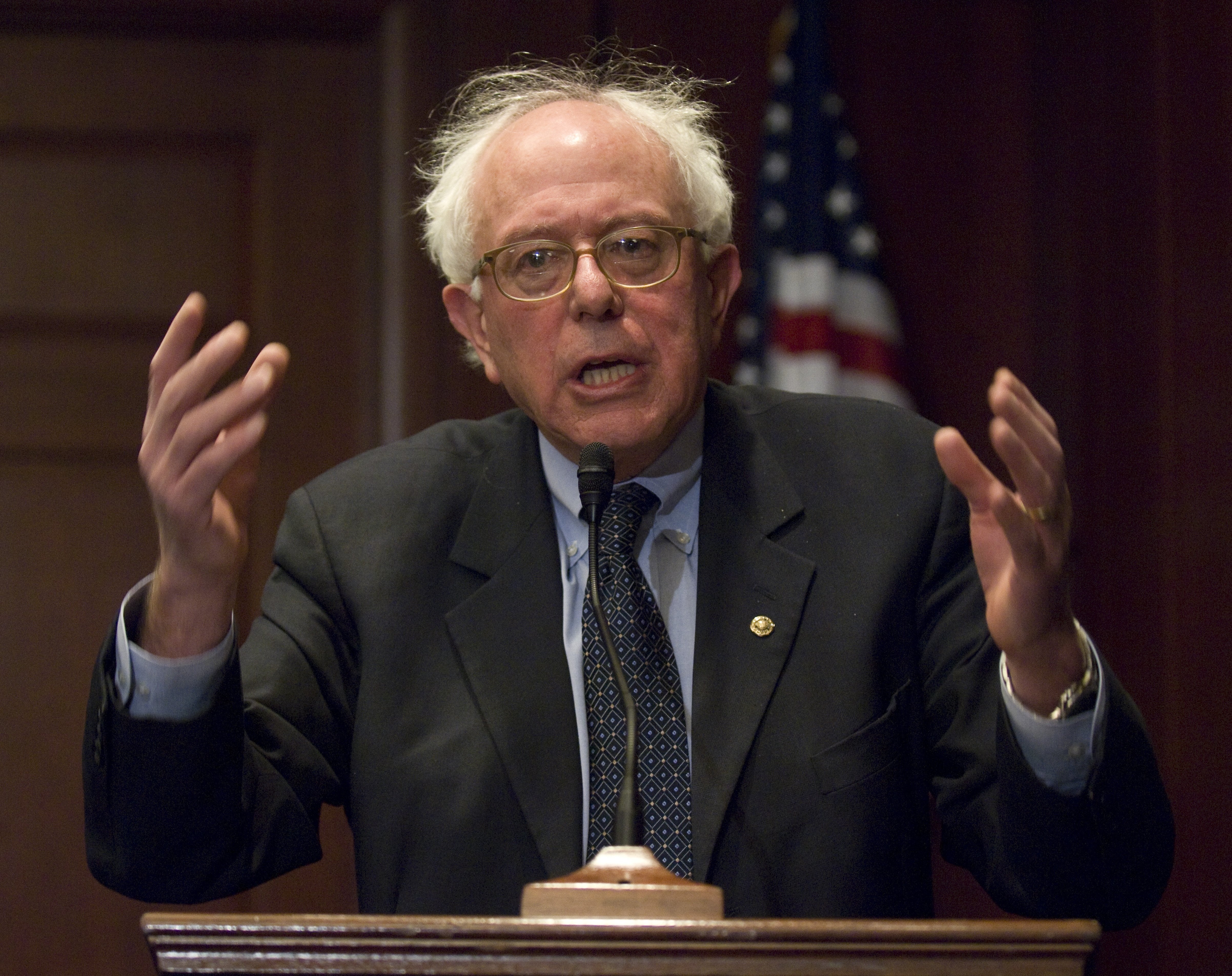 Bernie Sanders i dress holder tale ved et podium med et amerikansk flagg i bakgrunnen