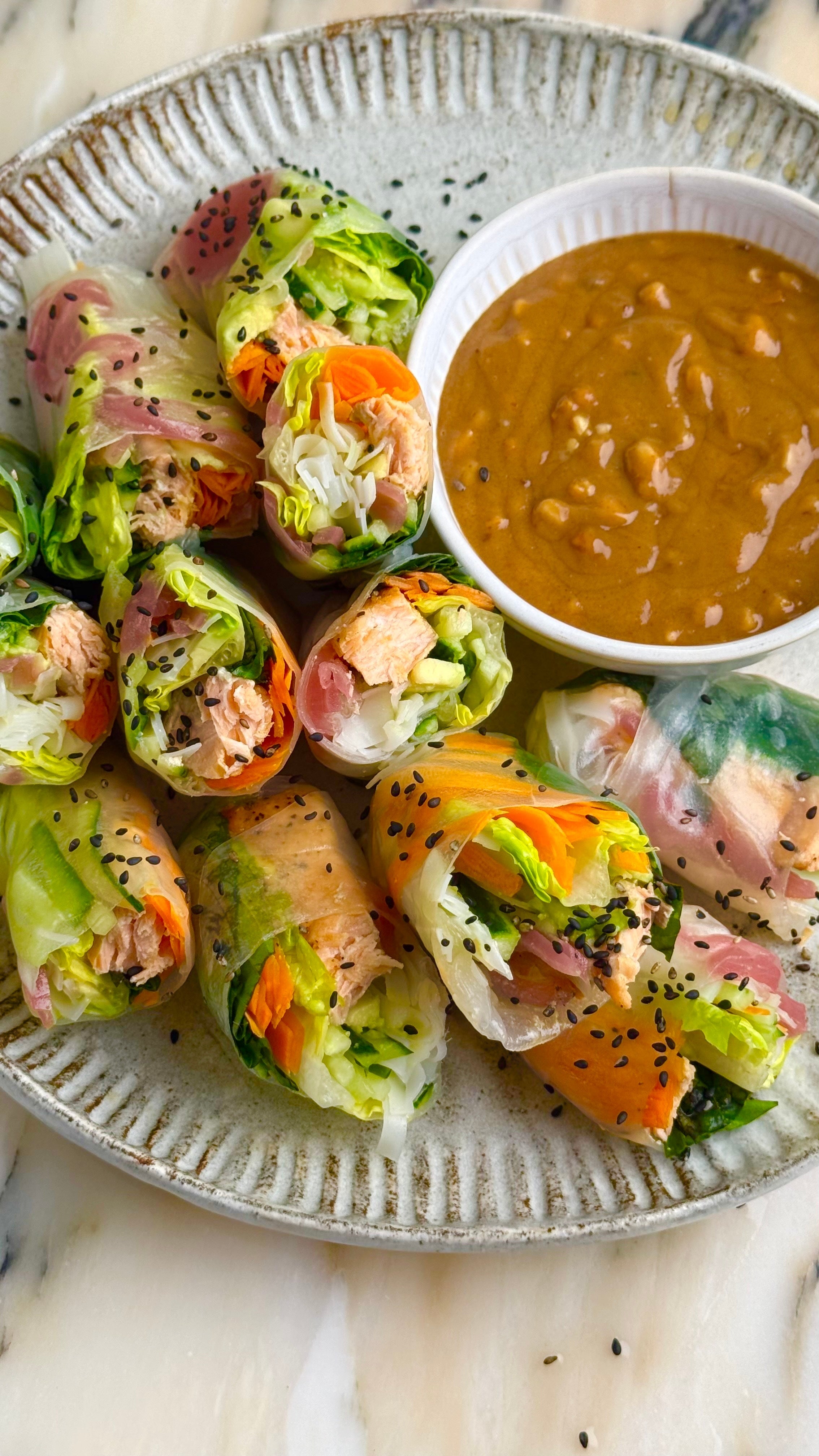 A plate of colorful fresh spring rolls filled with vegetables and protein, served with a bowl of peanut dipping sauce