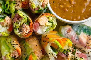 A plate of colorful fresh spring rolls filled with vegetables and protein, served with a bowl of peanut dipping sauce