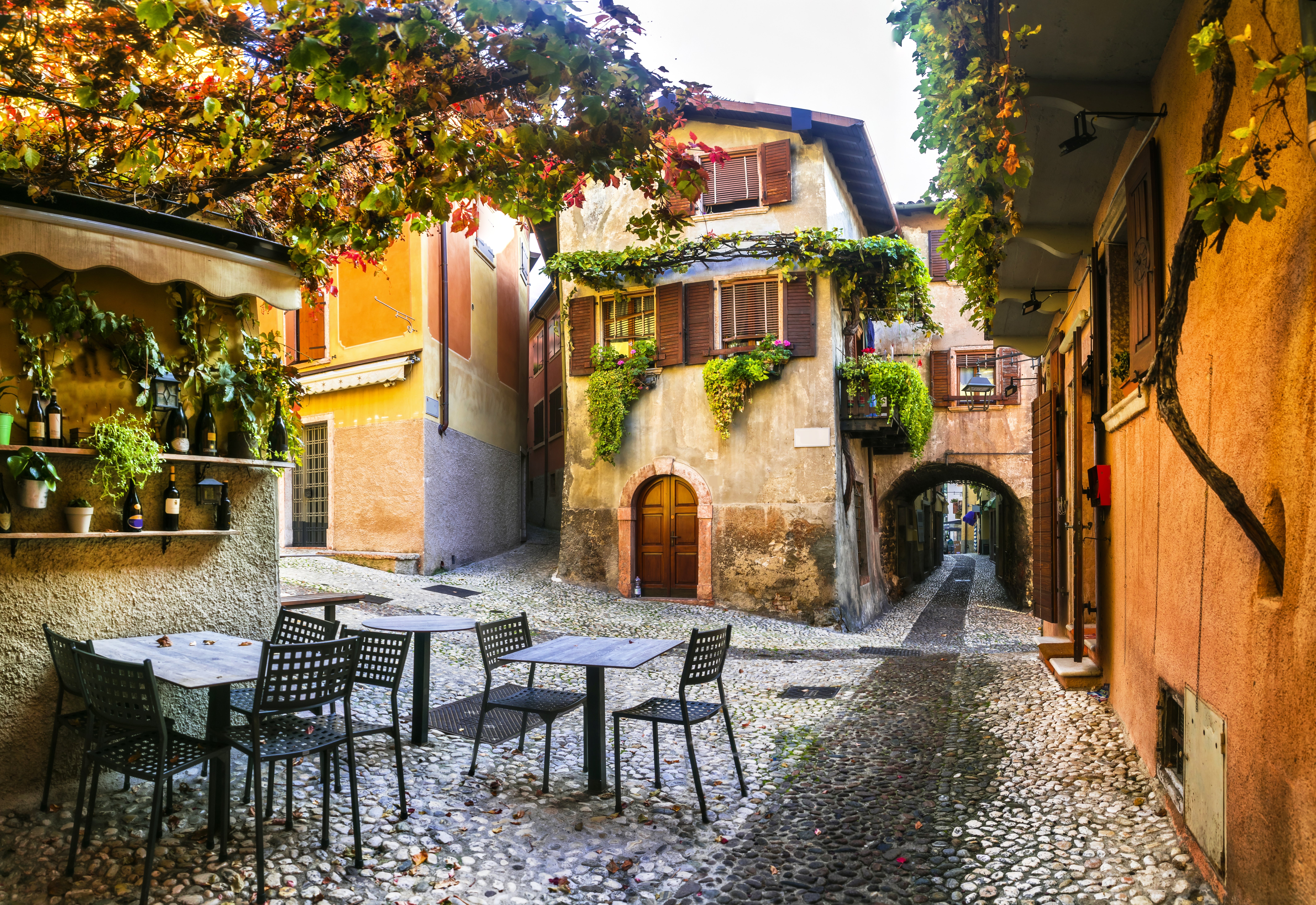 Charming cobblestone street in a quaint village with vine-covered buildings and empty outdoor café tables