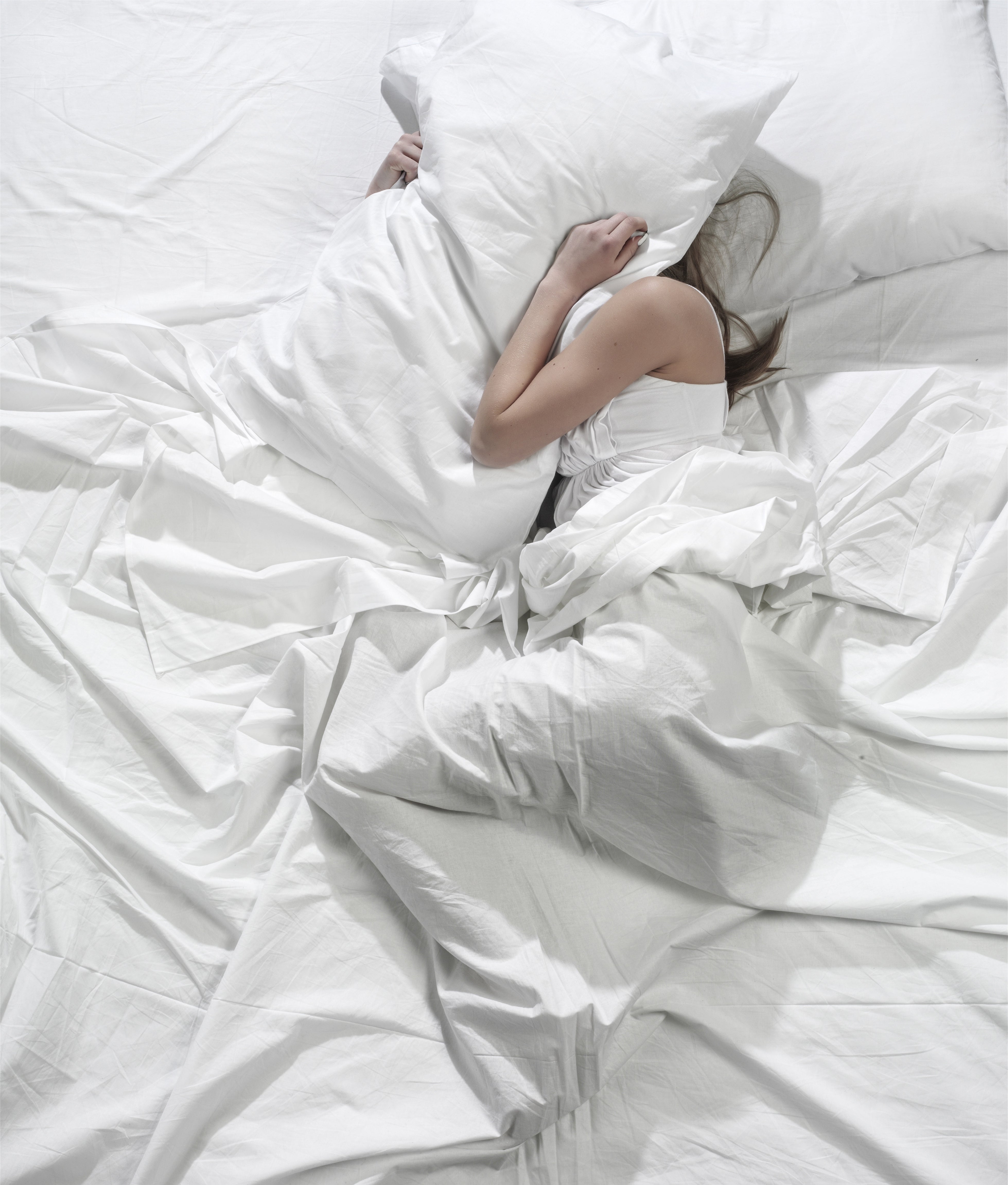 Person lying in a bed, covering face with a pillow. Relaxation or travel rest theme