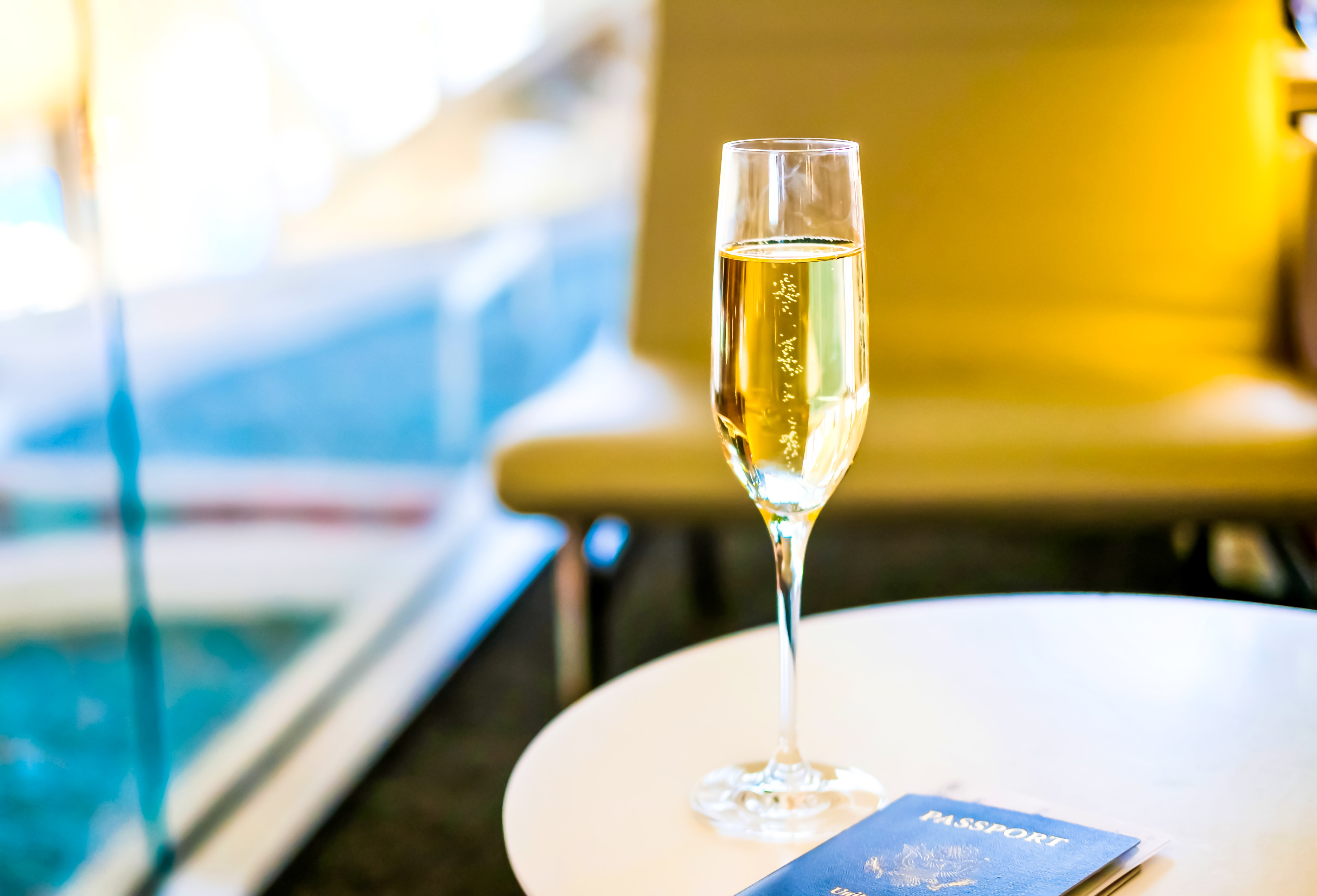 A glass of champagne and a passport on a table, suggesting luxury travel in an airport lounge setting
