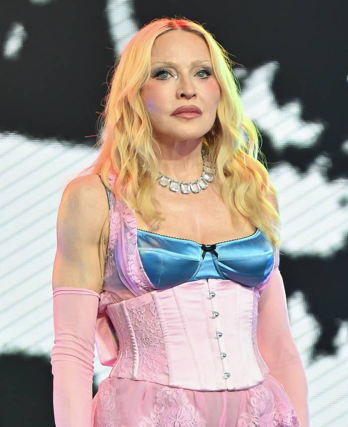 Person in a strapless pink lace dress with a blue satin top and long gloves, wearing a beaded necklace, standing on a stage