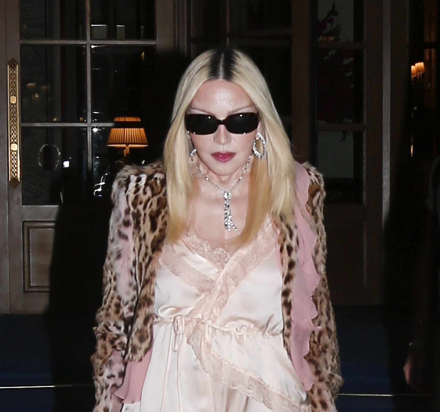 Person in lace outfit, leopard faux fur coat, fishnet stockings, and knee-high boots, wearing sunglasses, walking down steps