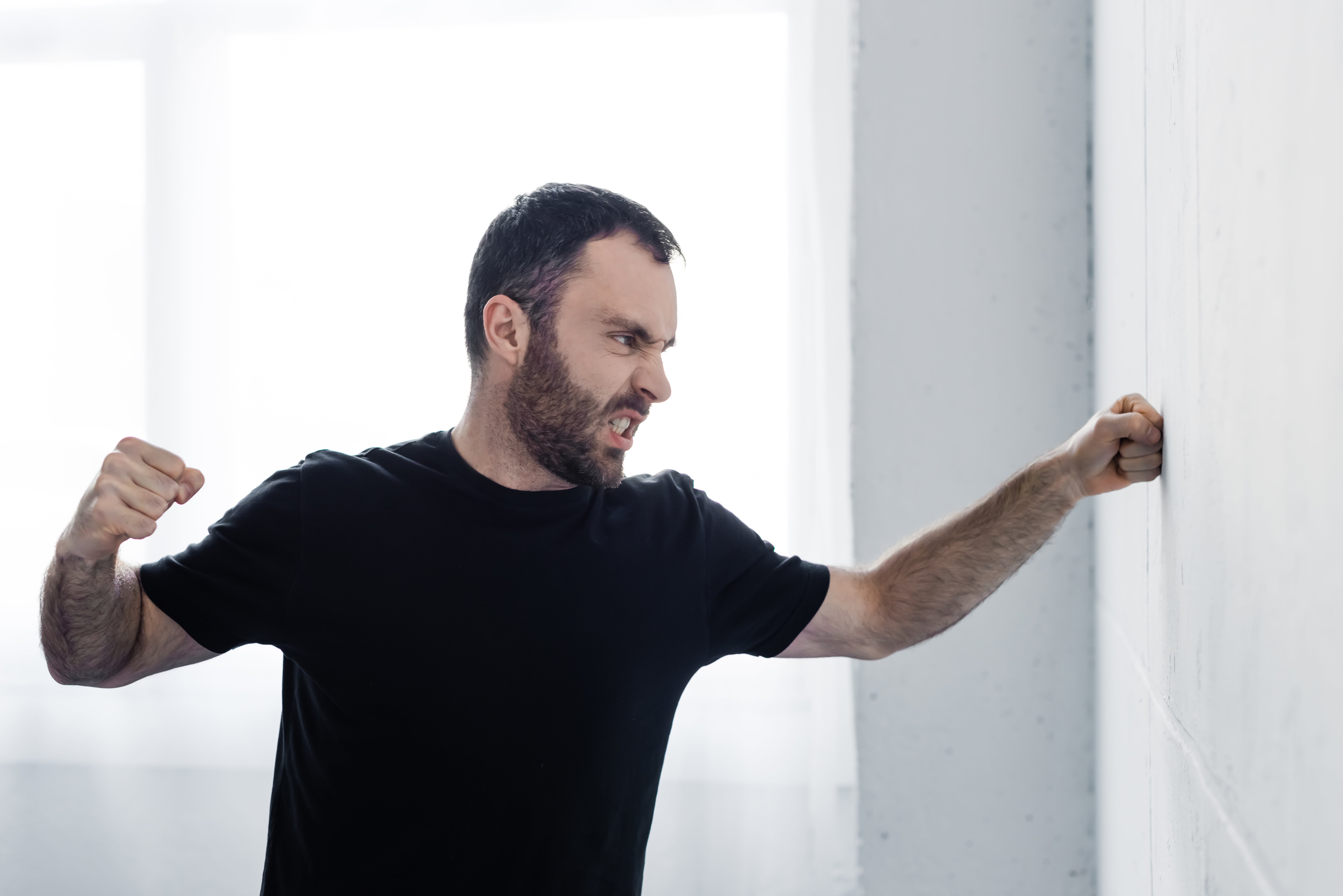 Man in a black shirt angrily punching a wall, showcasing emotional struggle