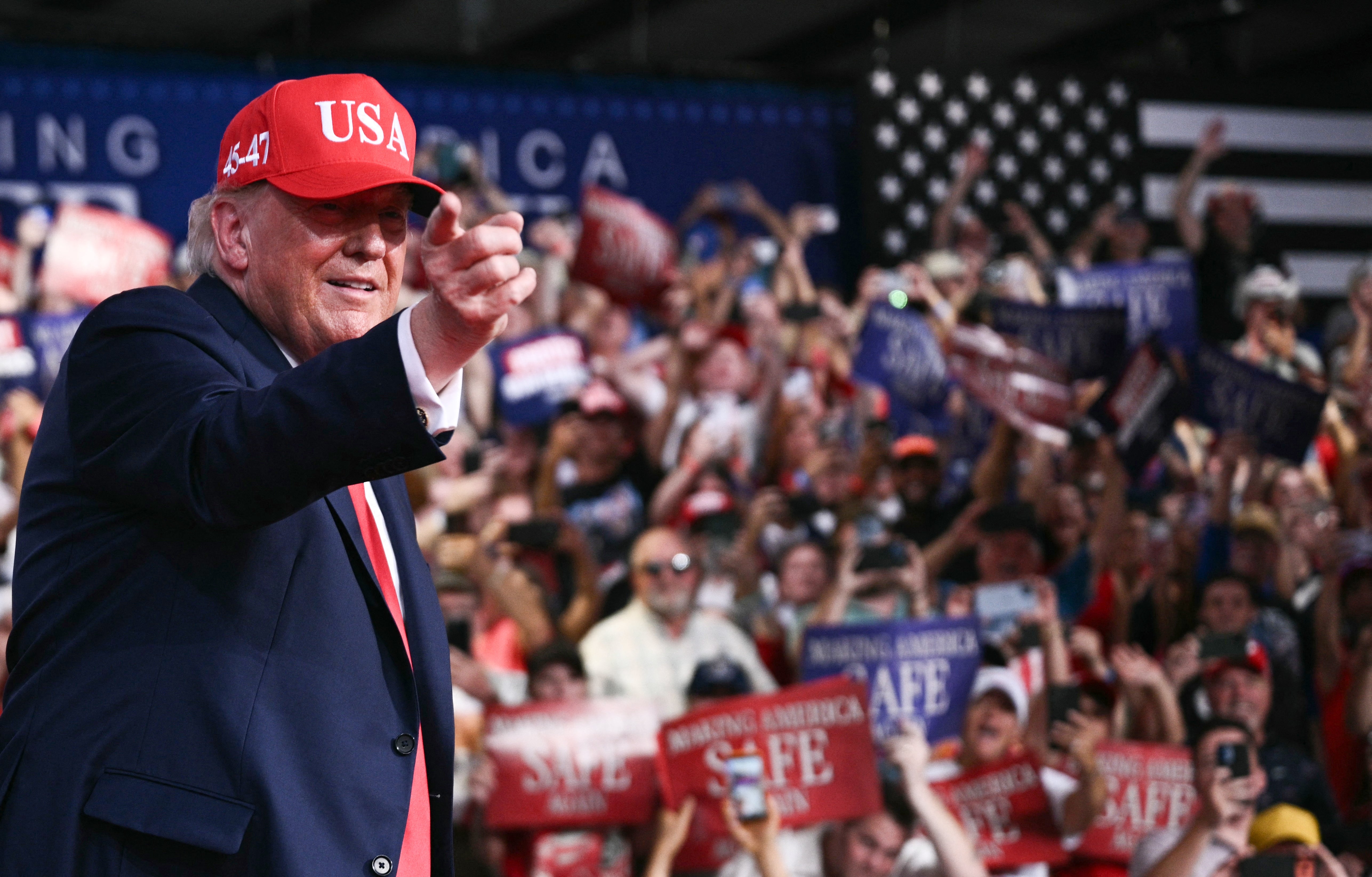 Person i et "USA" cap-bevegelser på et rally, omgitt av en jublende folkemengde som holder skilt med meldinger som