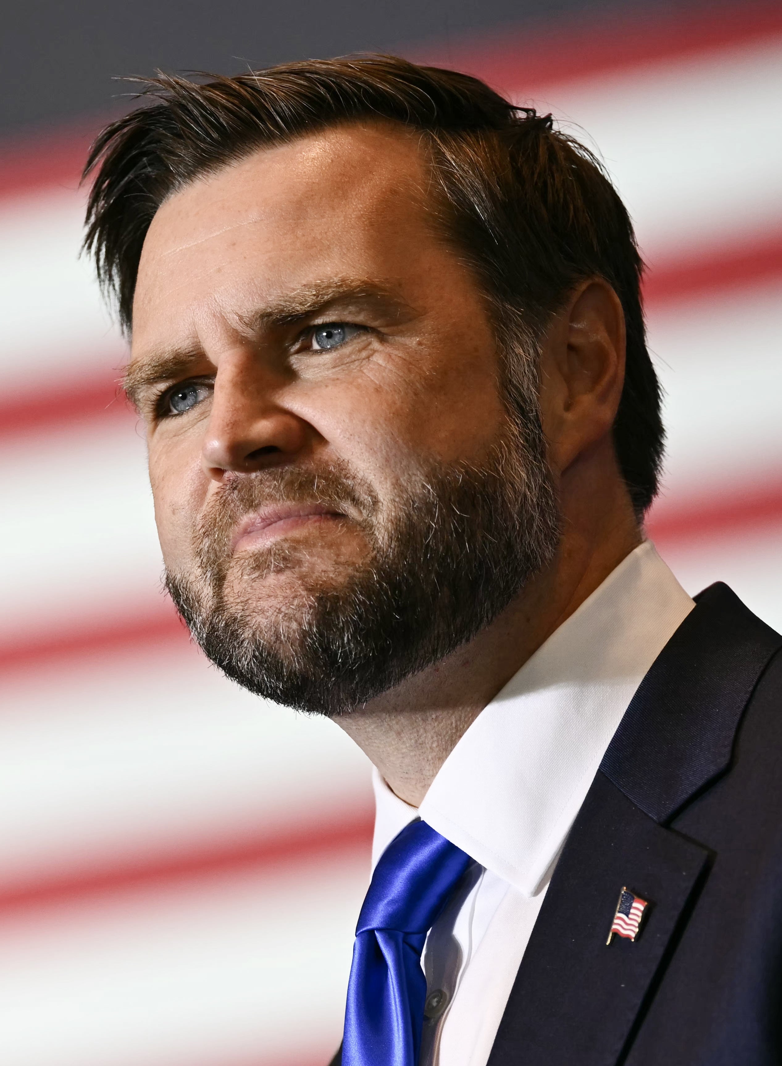 Mann i dress snakker på arrangementet, amerikansk flagg i bakgrunnen