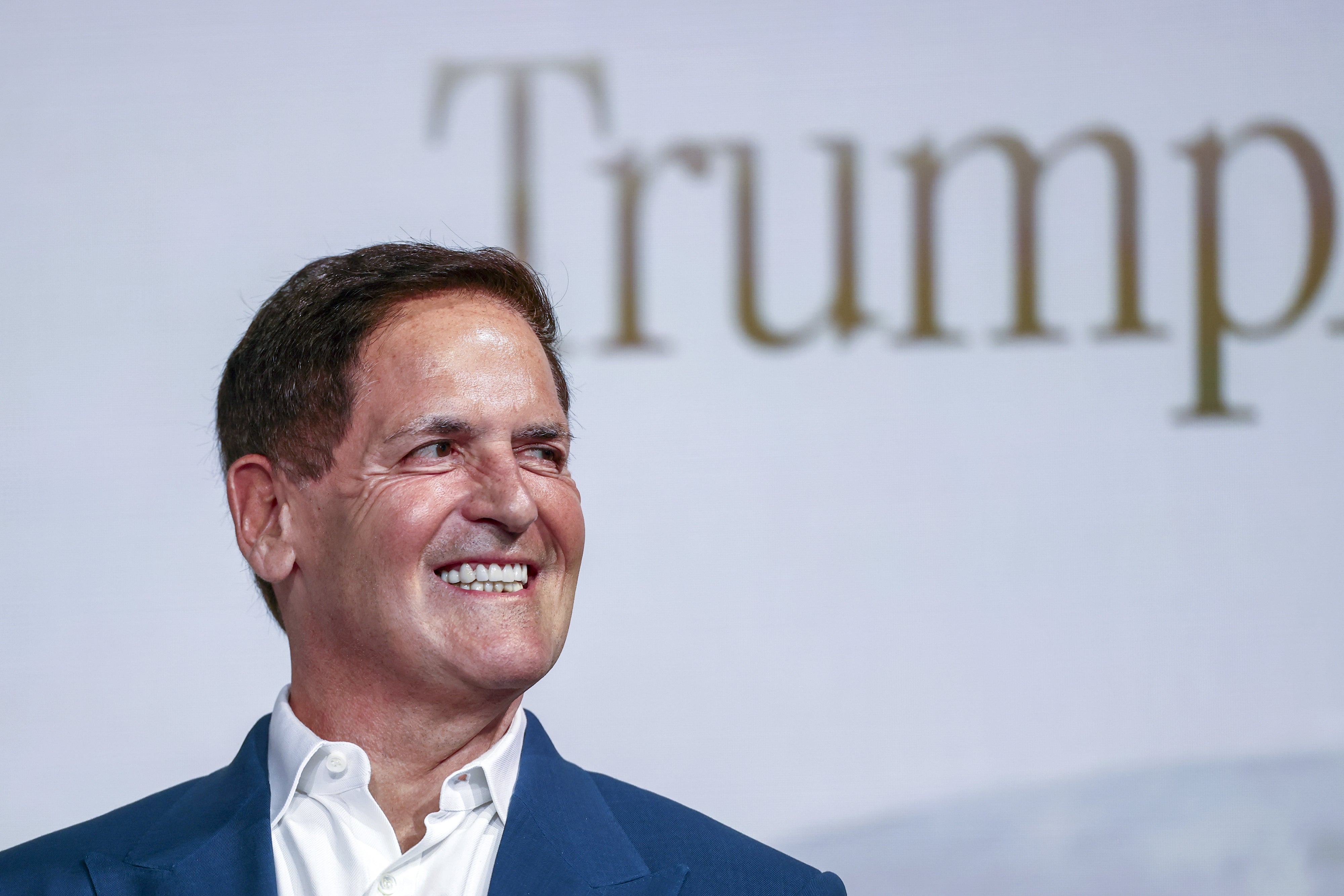 Man in suit smiling, standing in front of a background with large letters visible