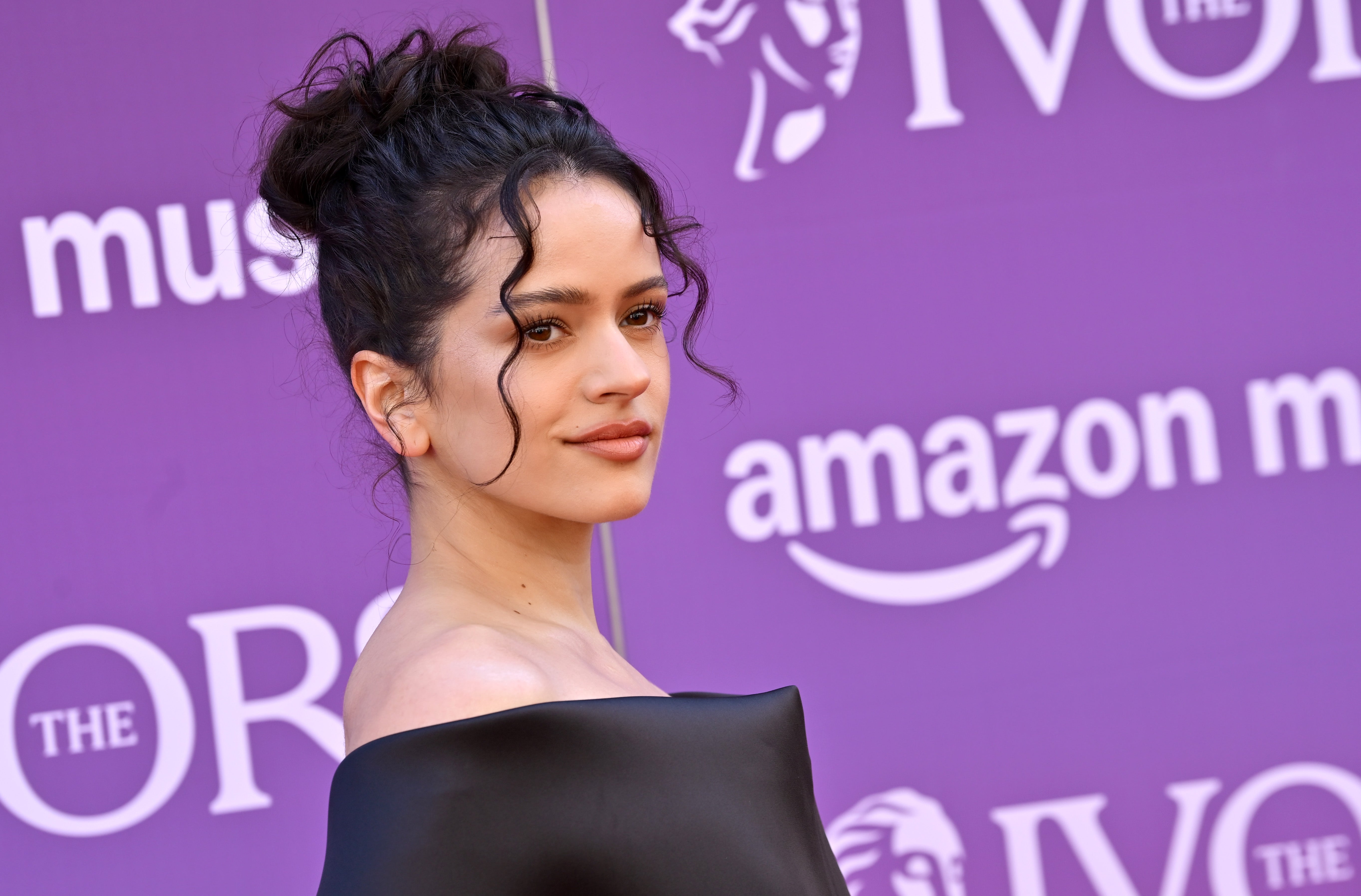 Person with updo hairstyle in off-shoulder dress poses at event with Amazon Music signage