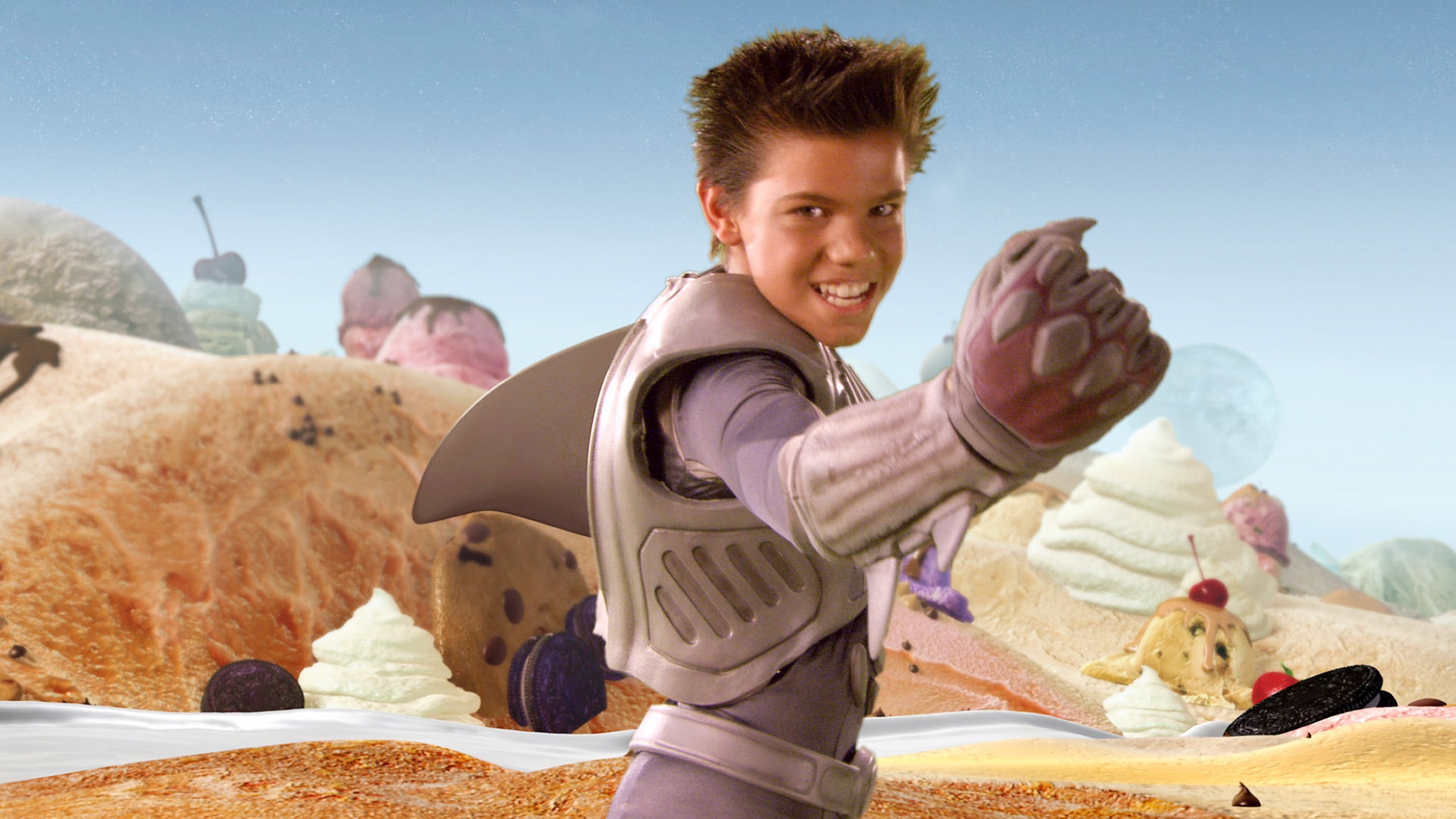 A person in a futuristic suit with a fin poses confidently in a candy-themed landscape